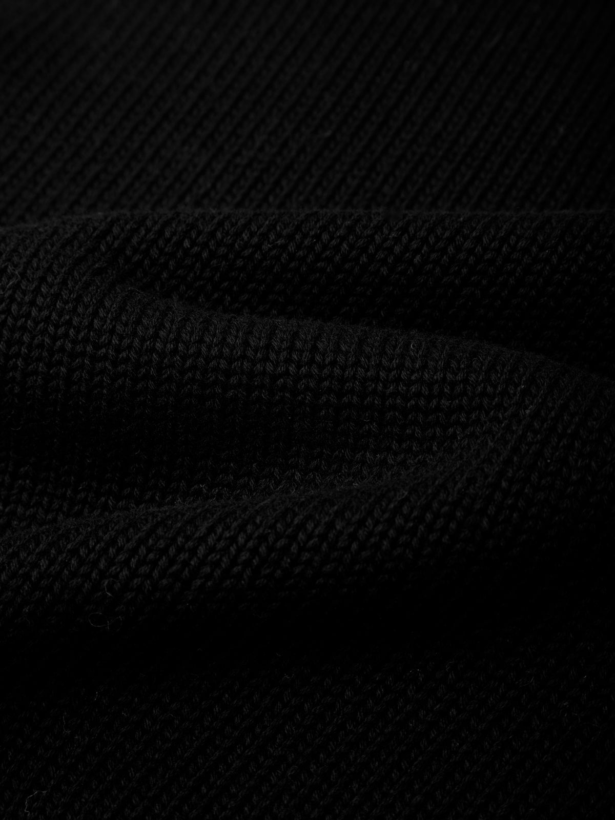 Close-up of a black textured knit fabric with soft folds and ribbed weave.