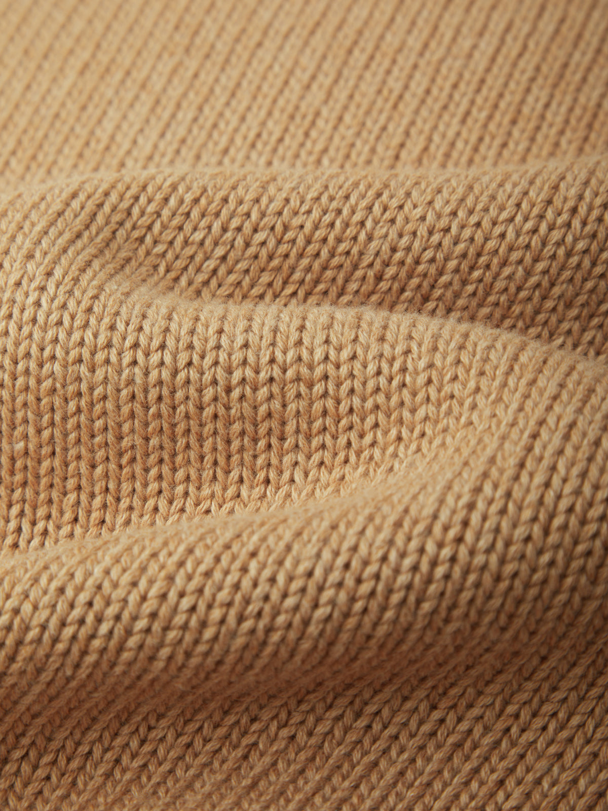 Close-up of a warm beige knit fabric with a ribbed texture and soft folds.