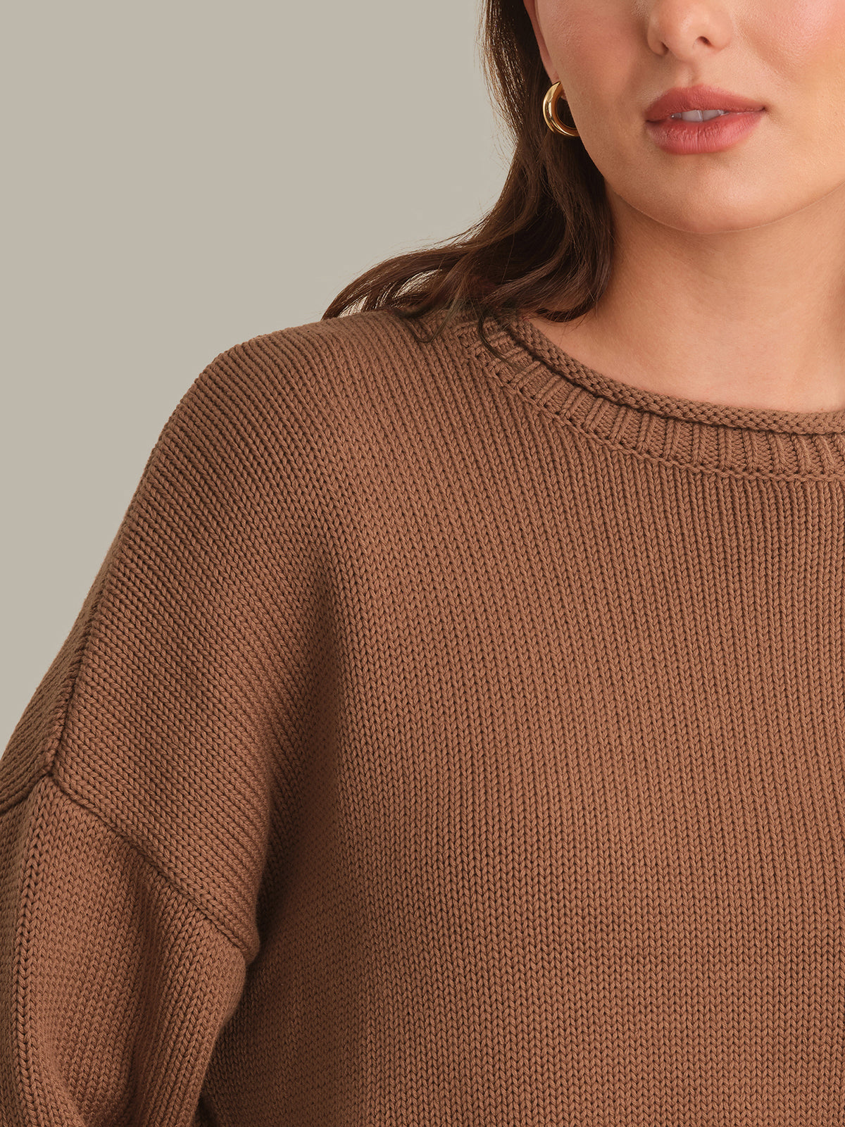 Close-up of a woman wearing a brown ribbed knit crewneck sweater, showing the texture of the fabric and the collar detail.