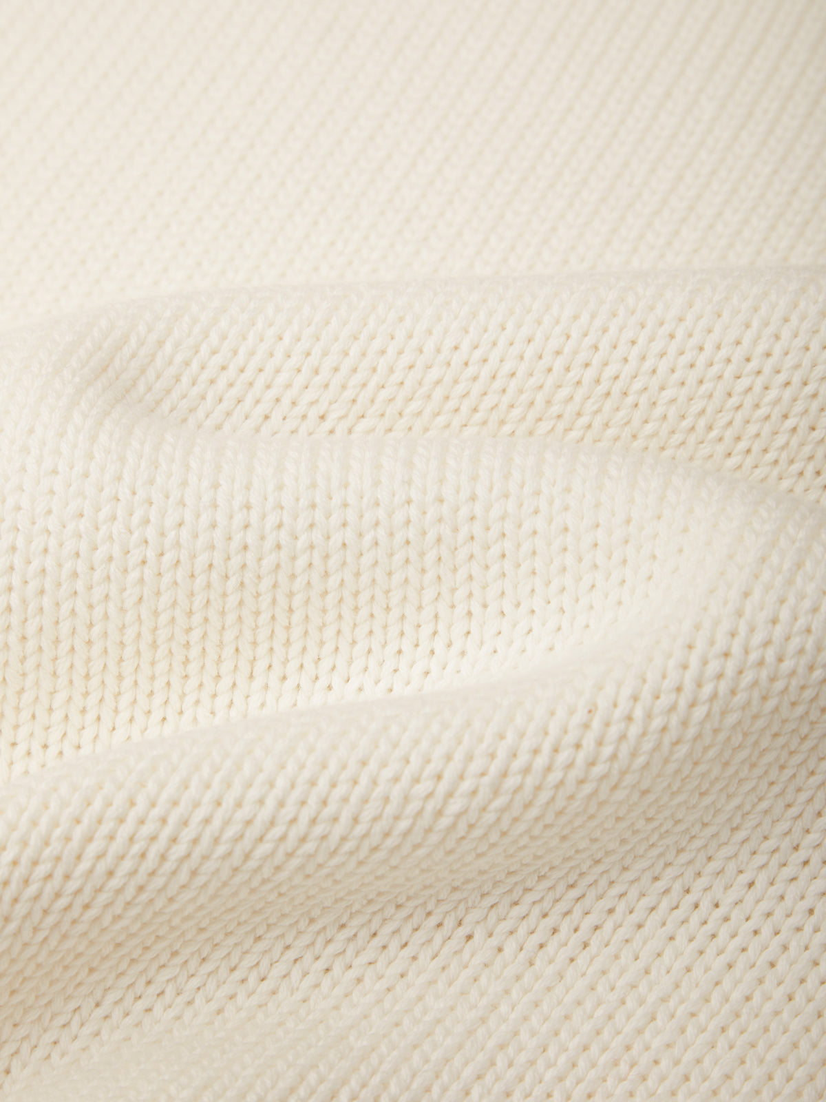 Close-up of a cream-colored knit fabric with a fine ribbed texture and soft folds.