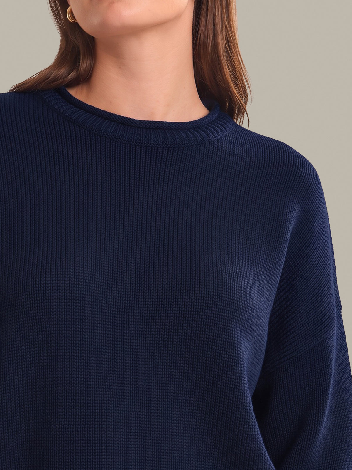 Close-up of a woman wearing a navy blue ribbed knit sweater against a solid beige background.