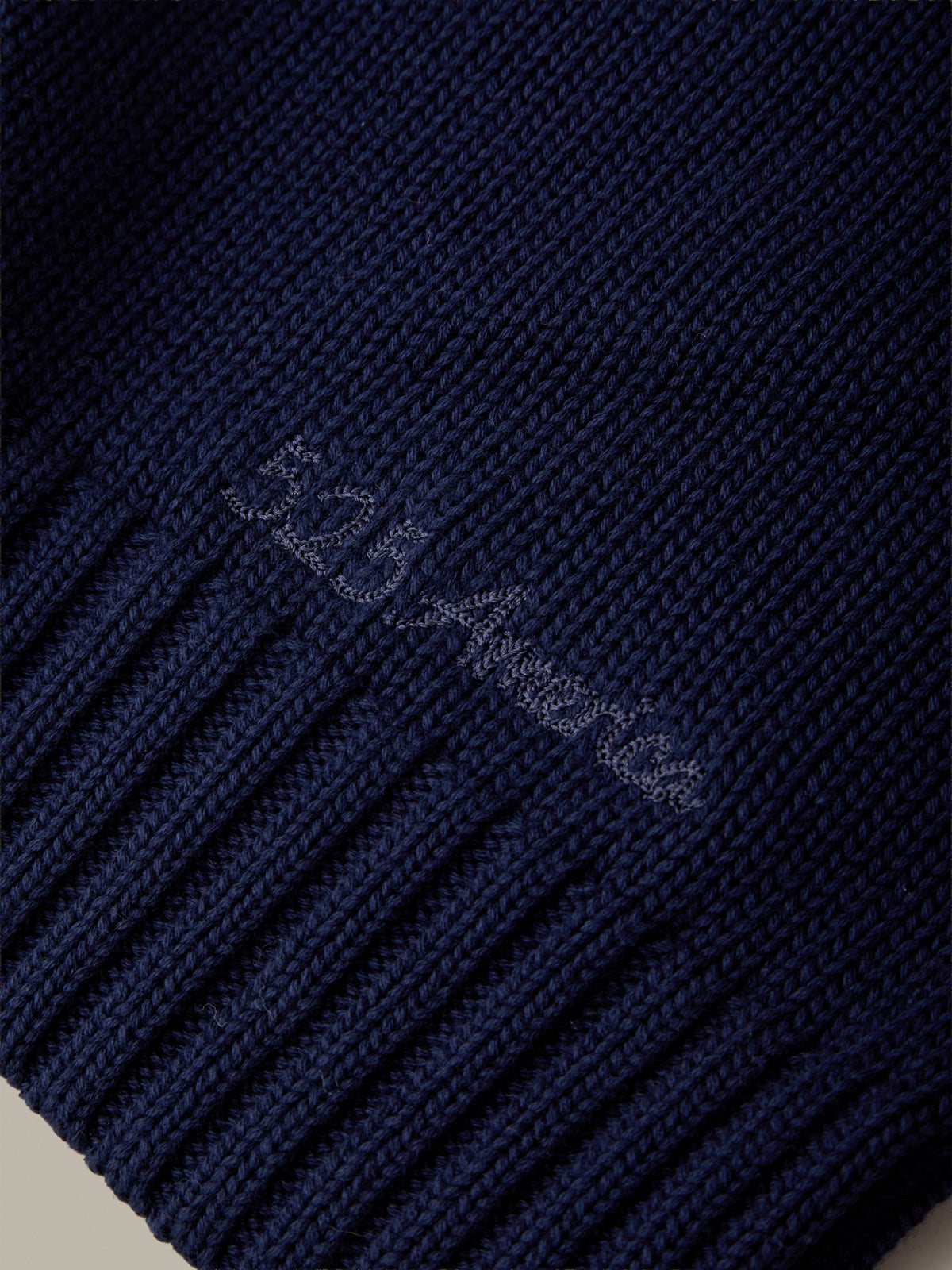 Close-up of a navy blue ribbed knit fabric with a subtle embroidered logo reading '525 America' in a lighter thread.