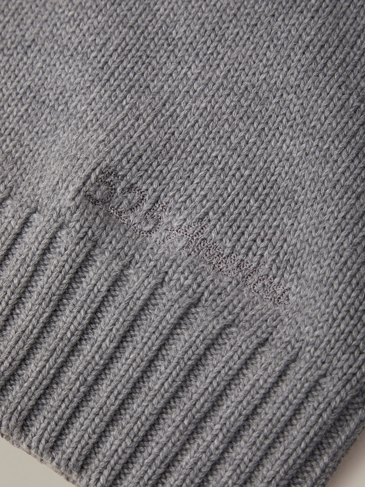 Close-up of a gray ribbed knit fabric with a tonal embroidered logo reading 'Dior' on the side.