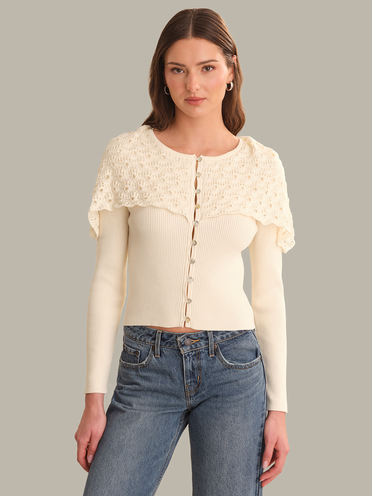 Woman wearing a cream-colored cardigan with lace sleeves on a gray background
