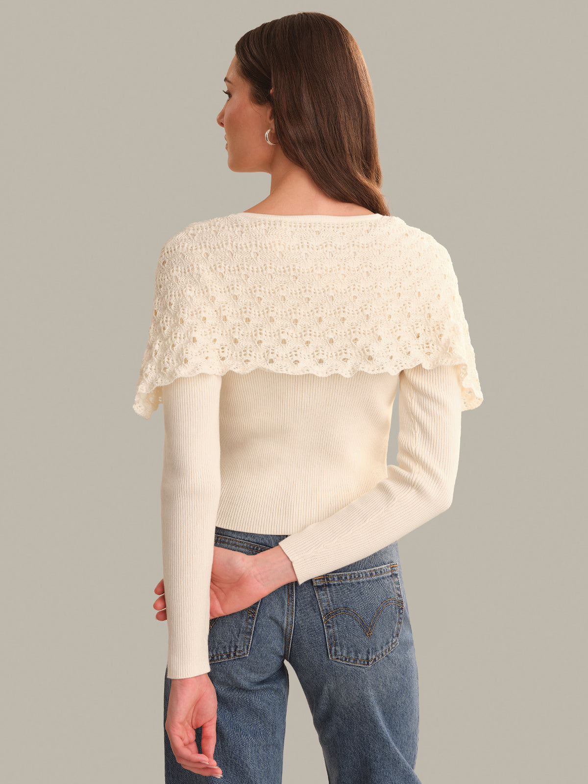 Woman wearing a cream-colored sweater with lace detailing on a gray background