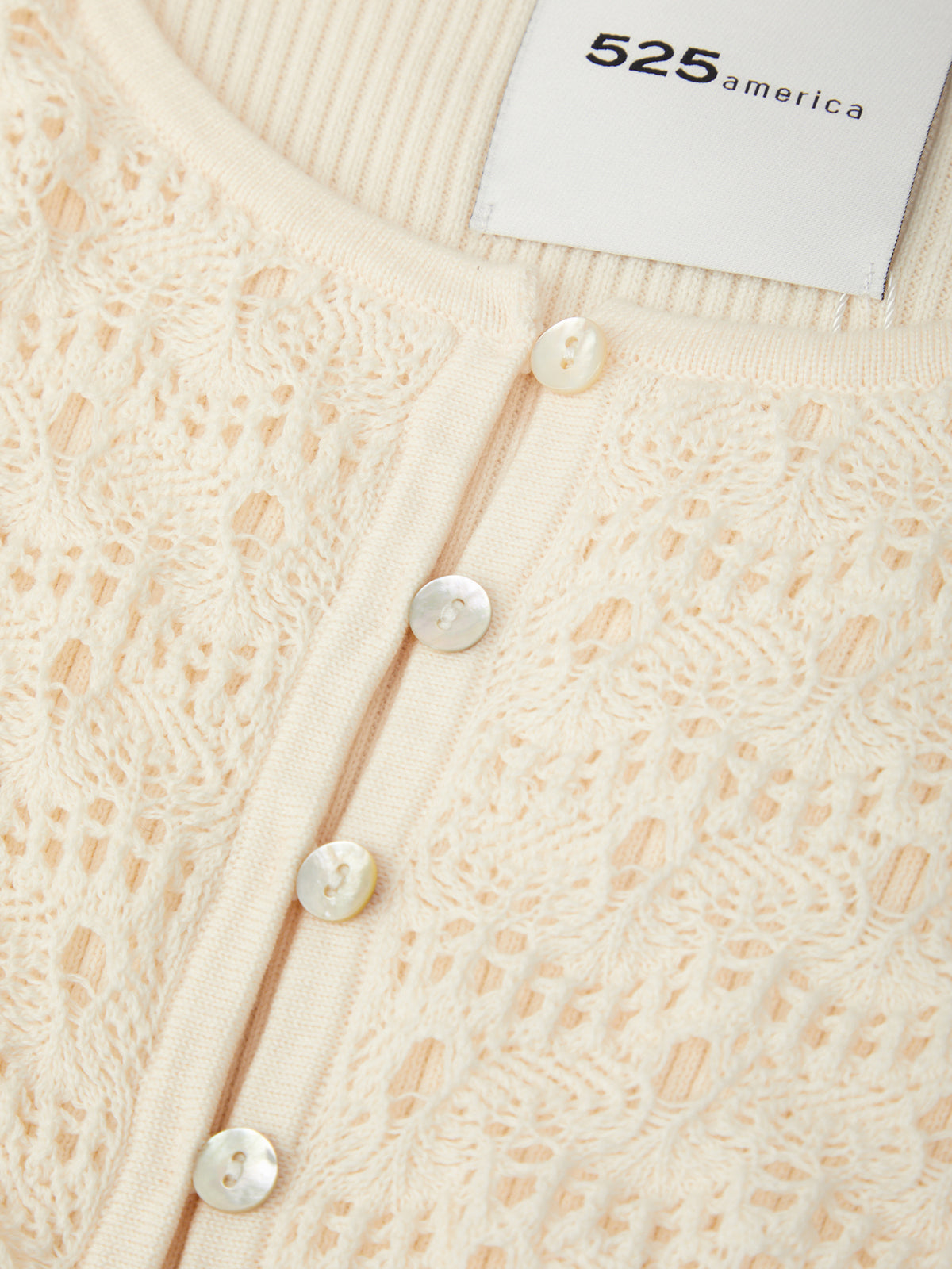 Close-up of a textured beige cardigan with pearl buttons and a brand label.