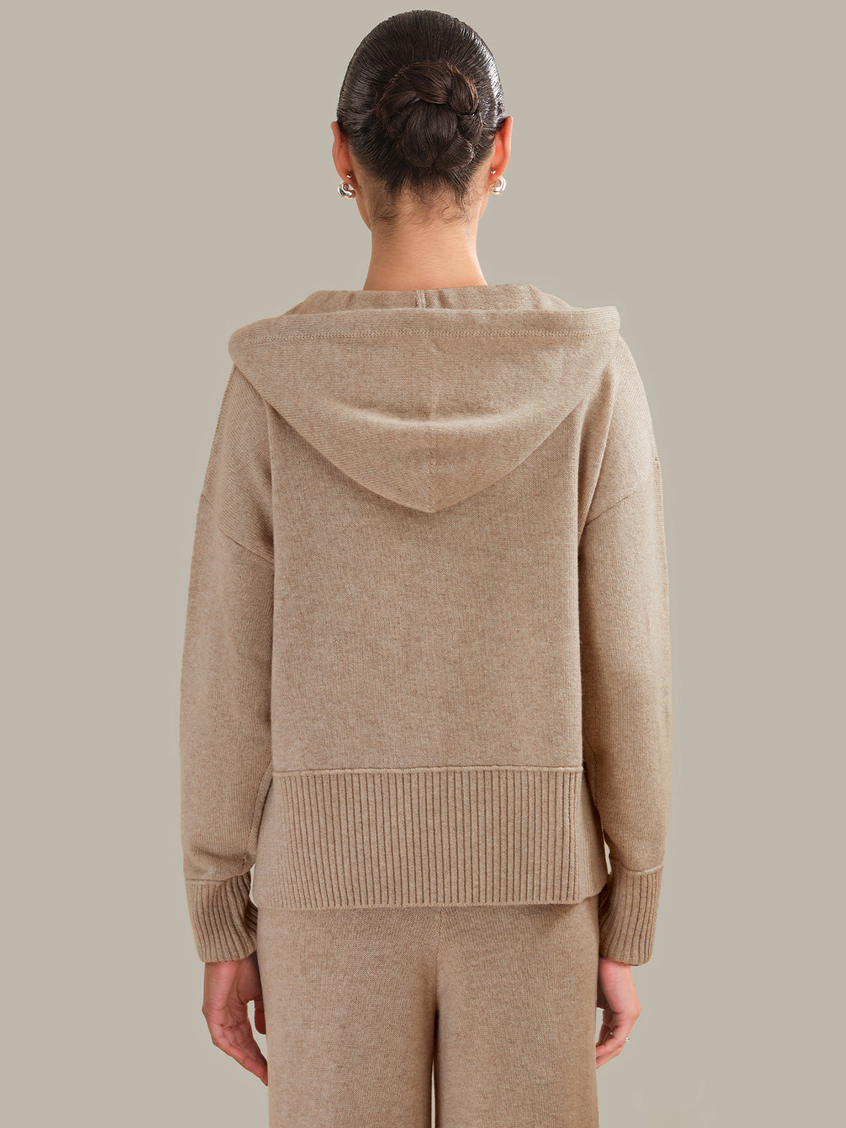 Person wearing a beige hoodie and pants on a plain background