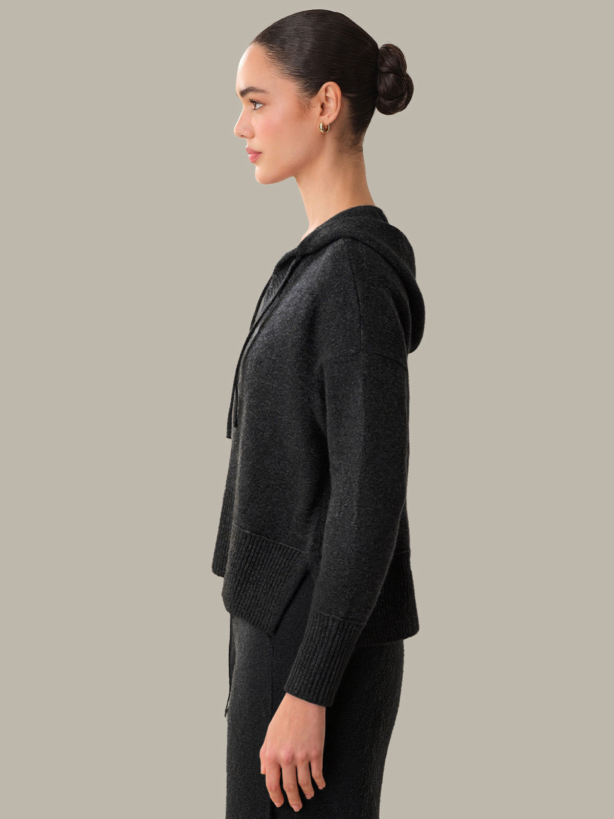 Woman wearing a dark gray hooded jacket against a neutral background