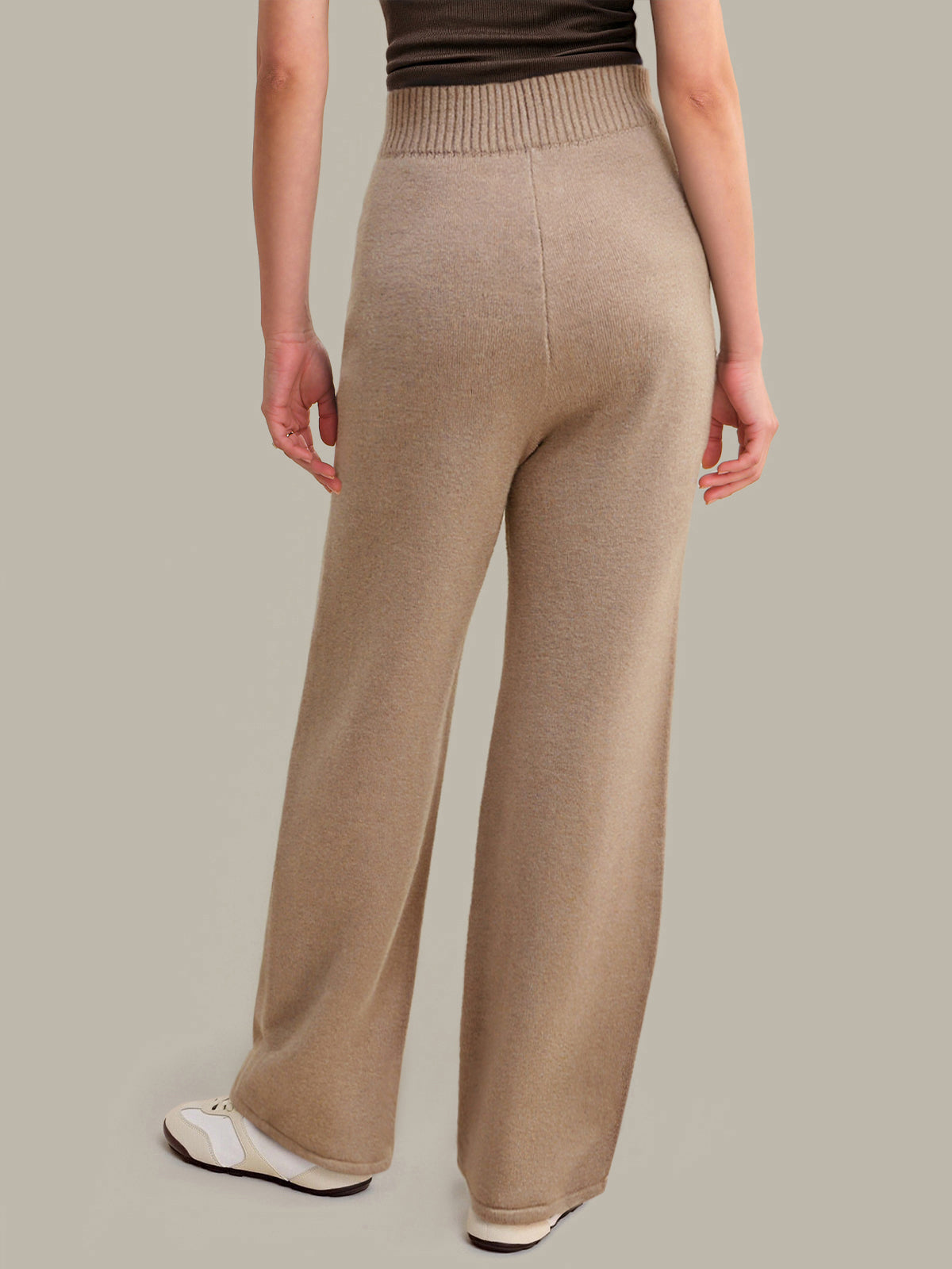 Person wearing beige knitted pants on a plain background