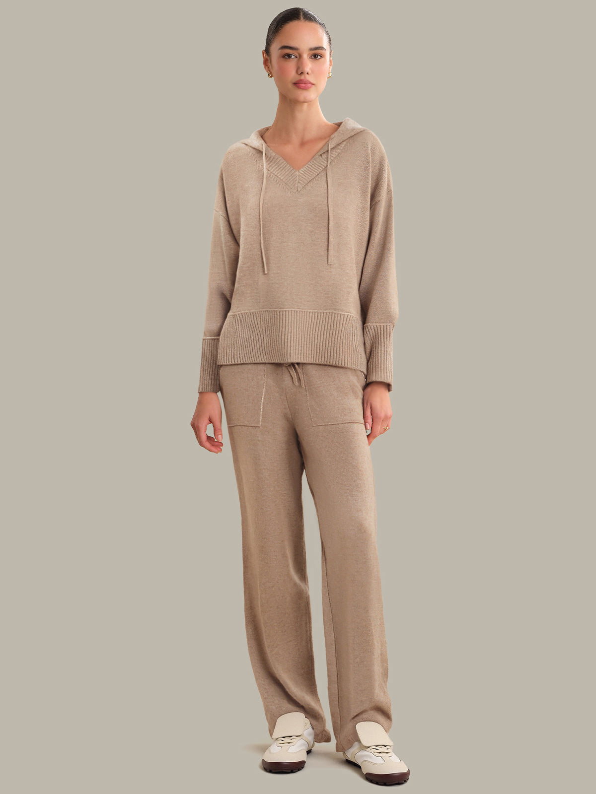 Woman wearing a beige sweater and pants set on a plain background