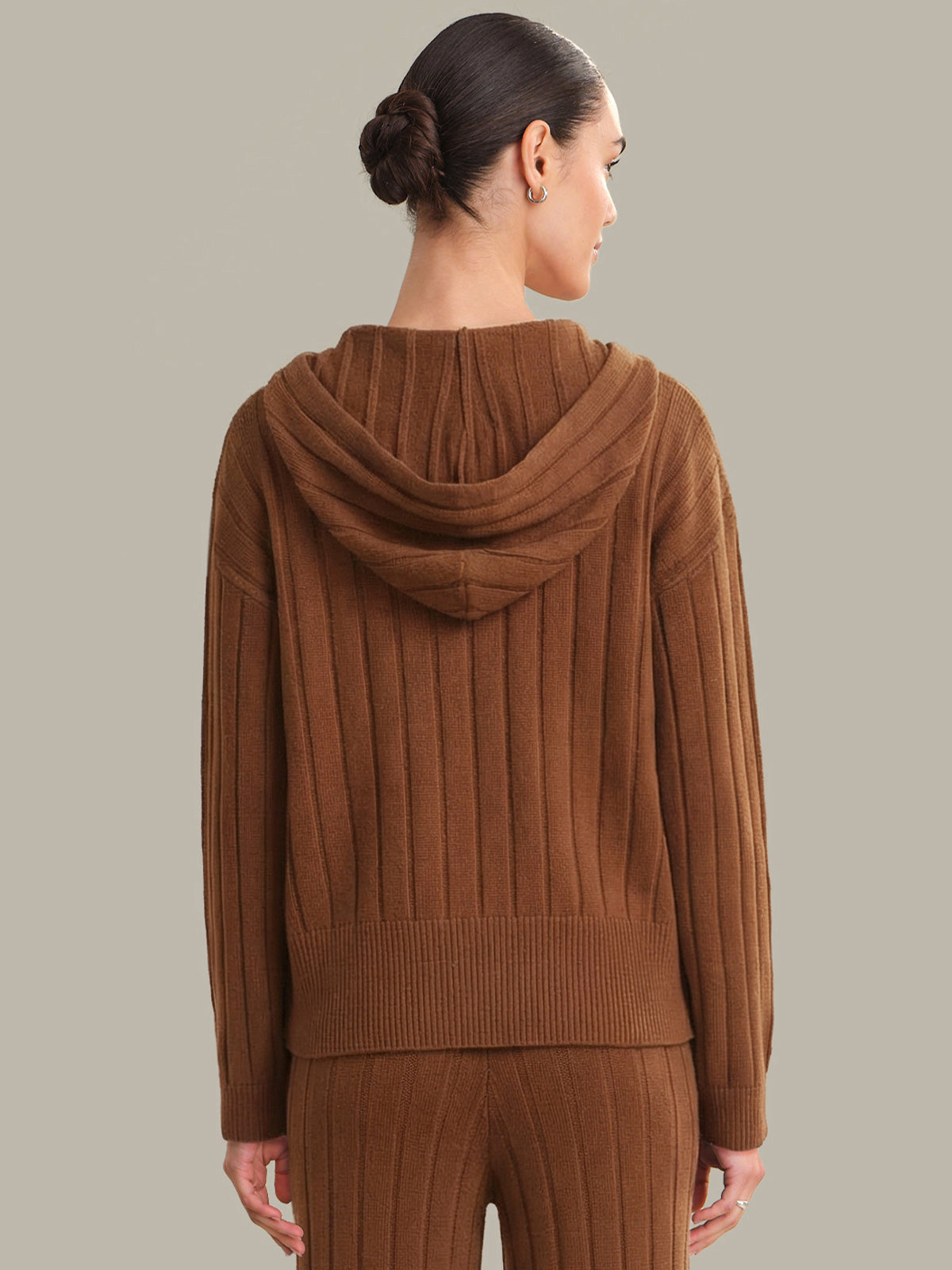 Woman wearing a brown ribbed knit hoodie and pants on a plain background
