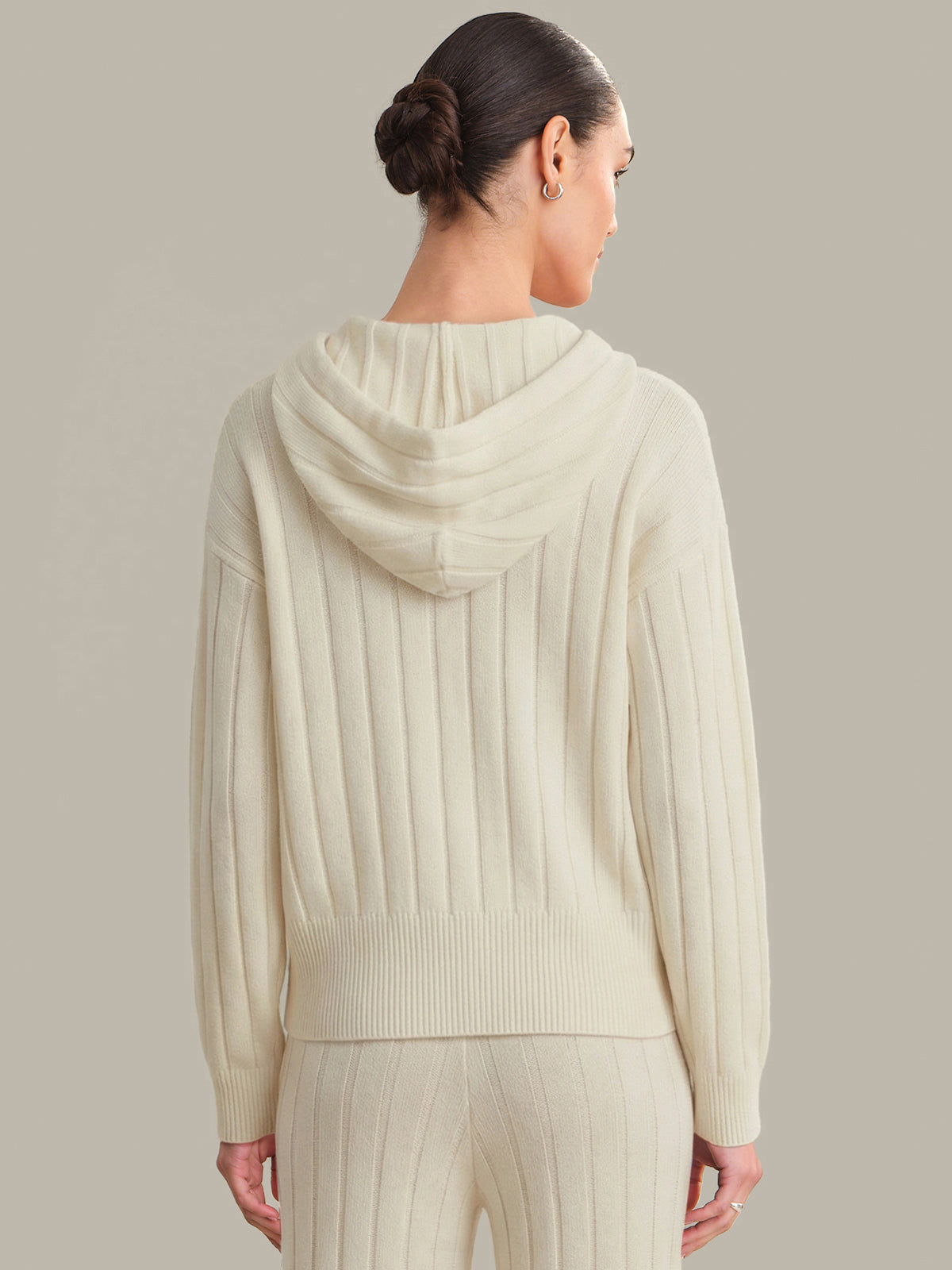 Woman wearing a cream-colored ribbed sweater and pants against a neutral background