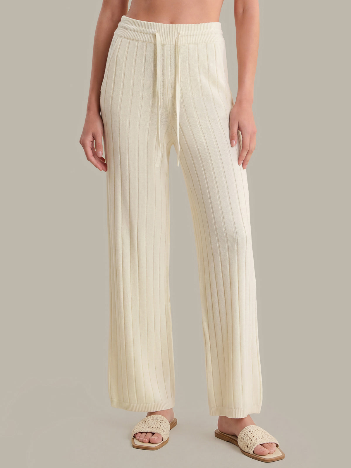 Person wearing cream pleated pants on a neutral background