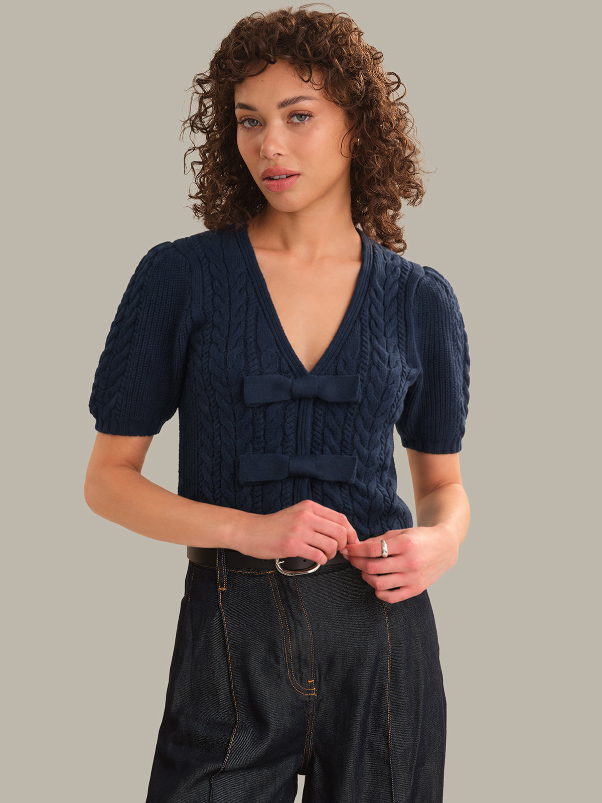 Woman wearing a navy blue cable knit top with a bow detail on a plain background