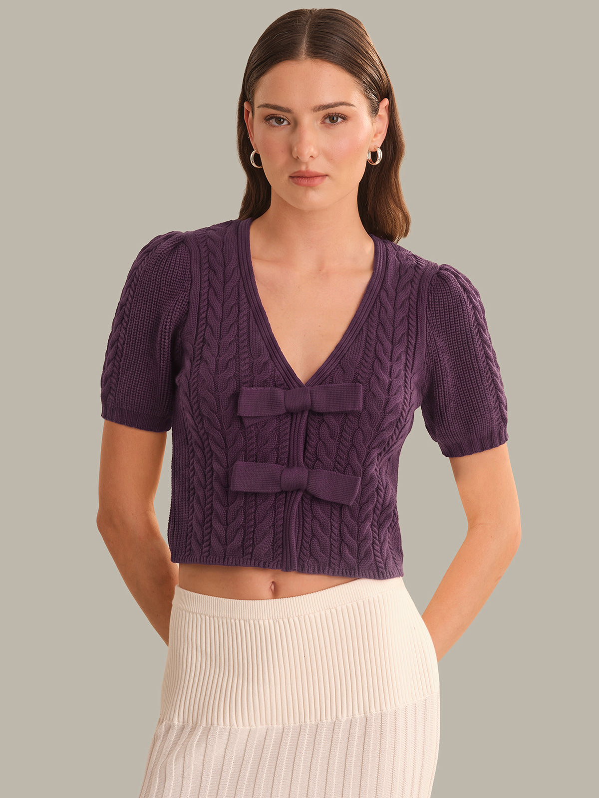 Woman wearing a purple cable knit top with puff sleeves on a gray background
