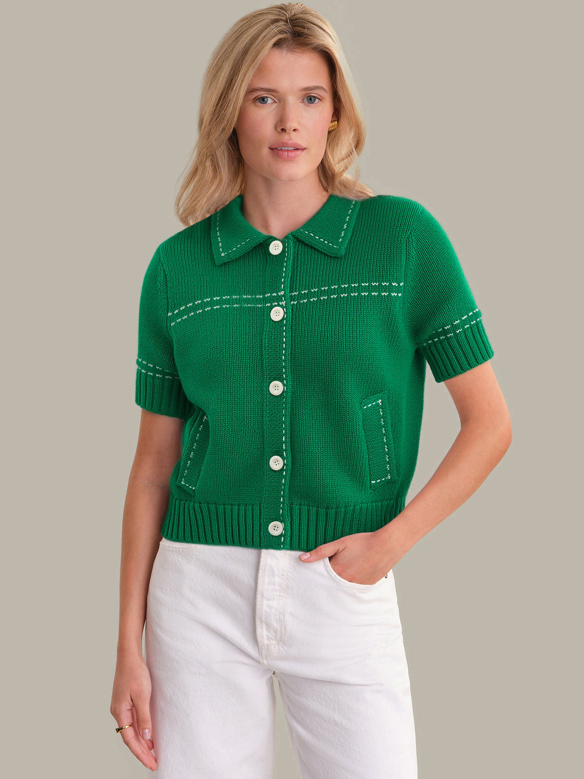 Woman wearing a green knitted short-sleeve cardigan with white pants on a neutral background