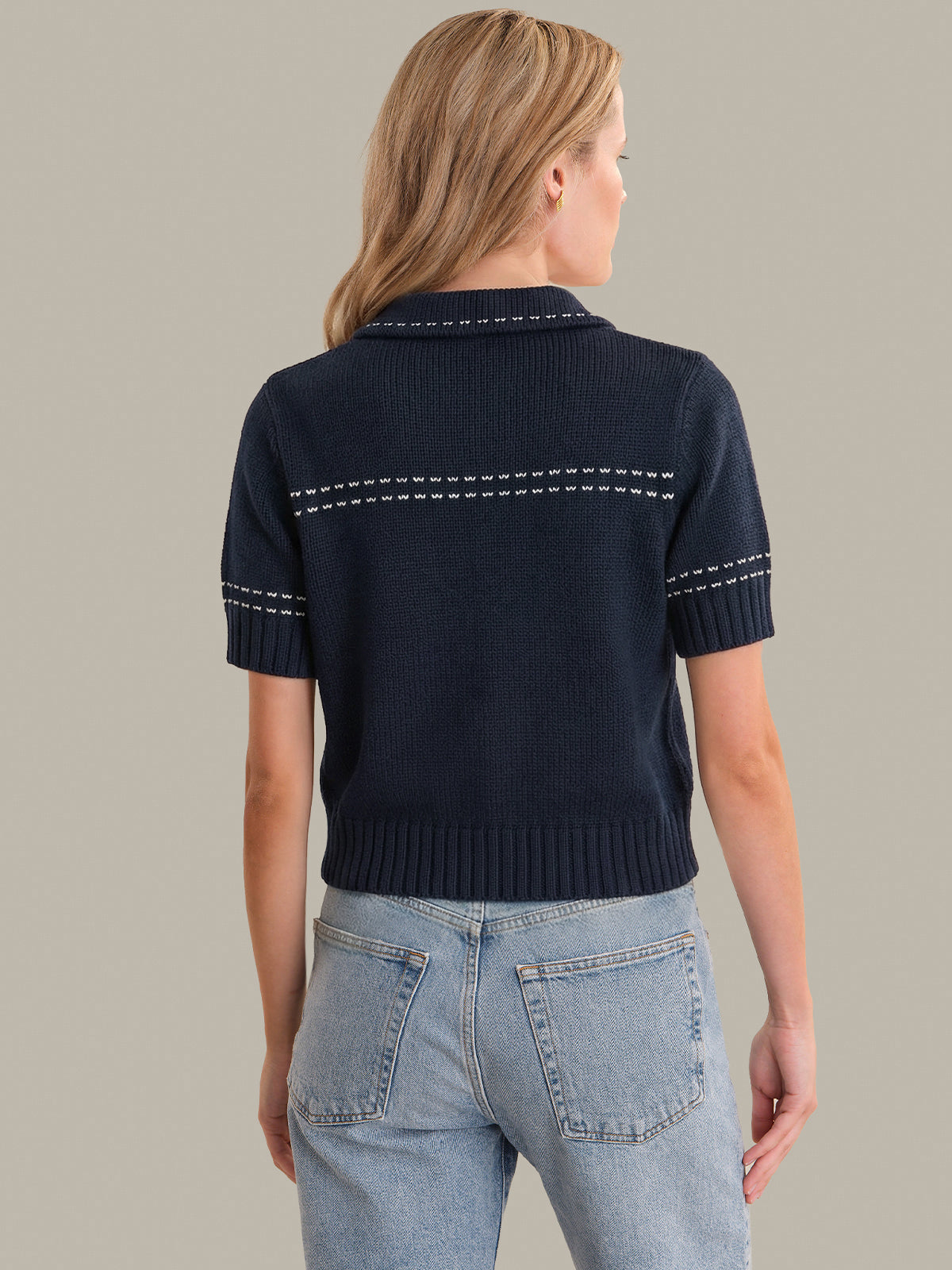 Woman wearing a navy blue cardigan with white stitching details on a neutral background