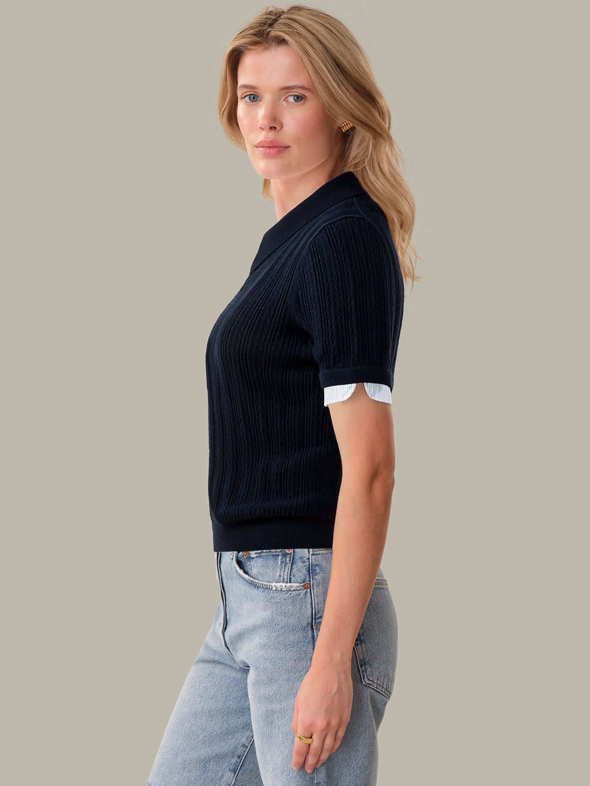 Woman wearing a black ribbed sweater and light blue jeans against a neutral background