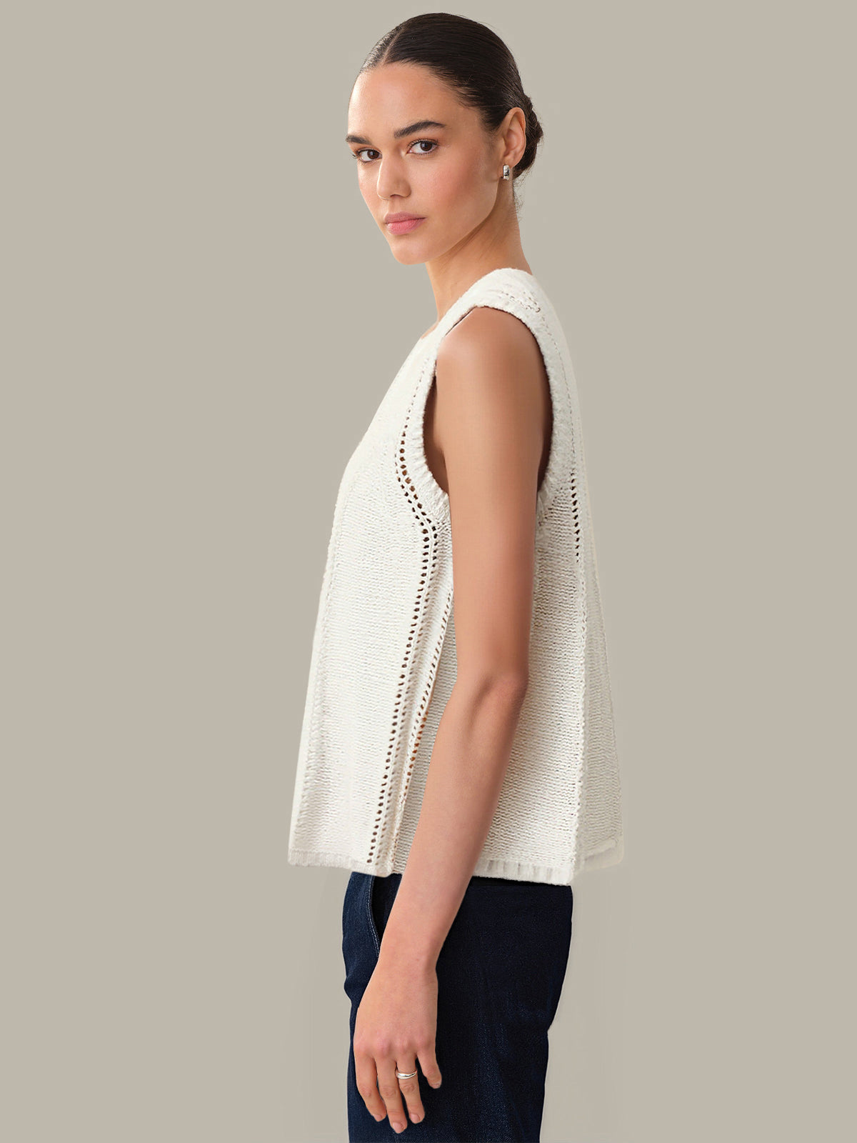 Woman wearing a white sleeveless top with lace details on a neutral background