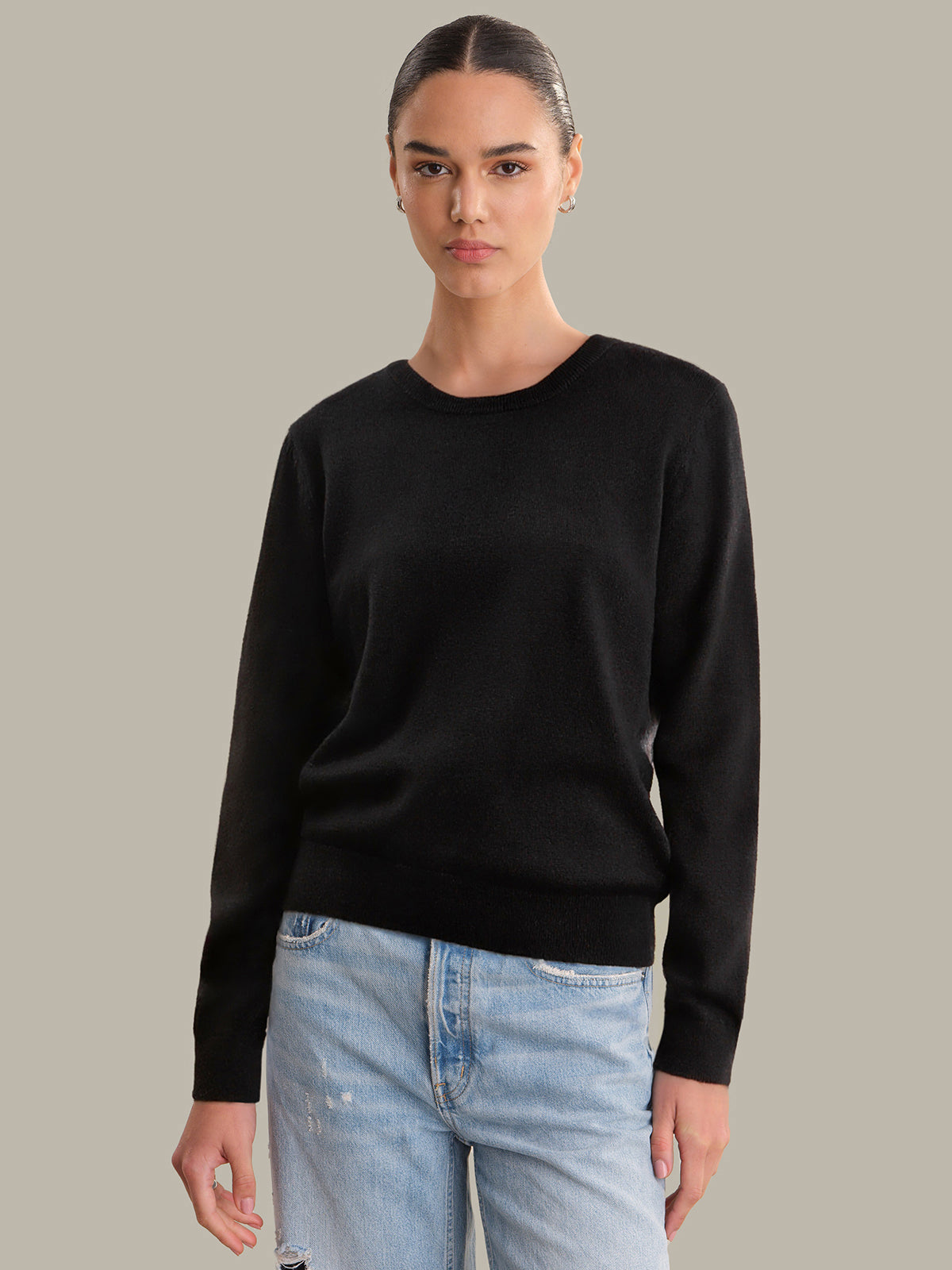 Person wearing a black sweater and light blue jeans on a gray background