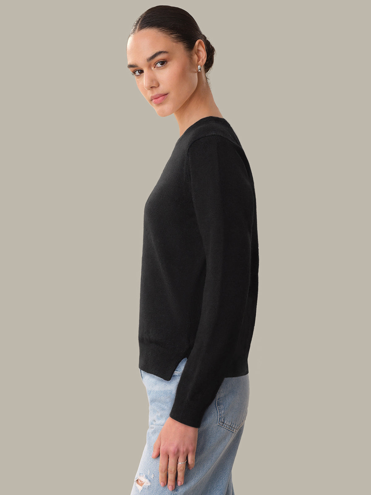 Woman wearing a black sweater and light blue jeans against a gray background