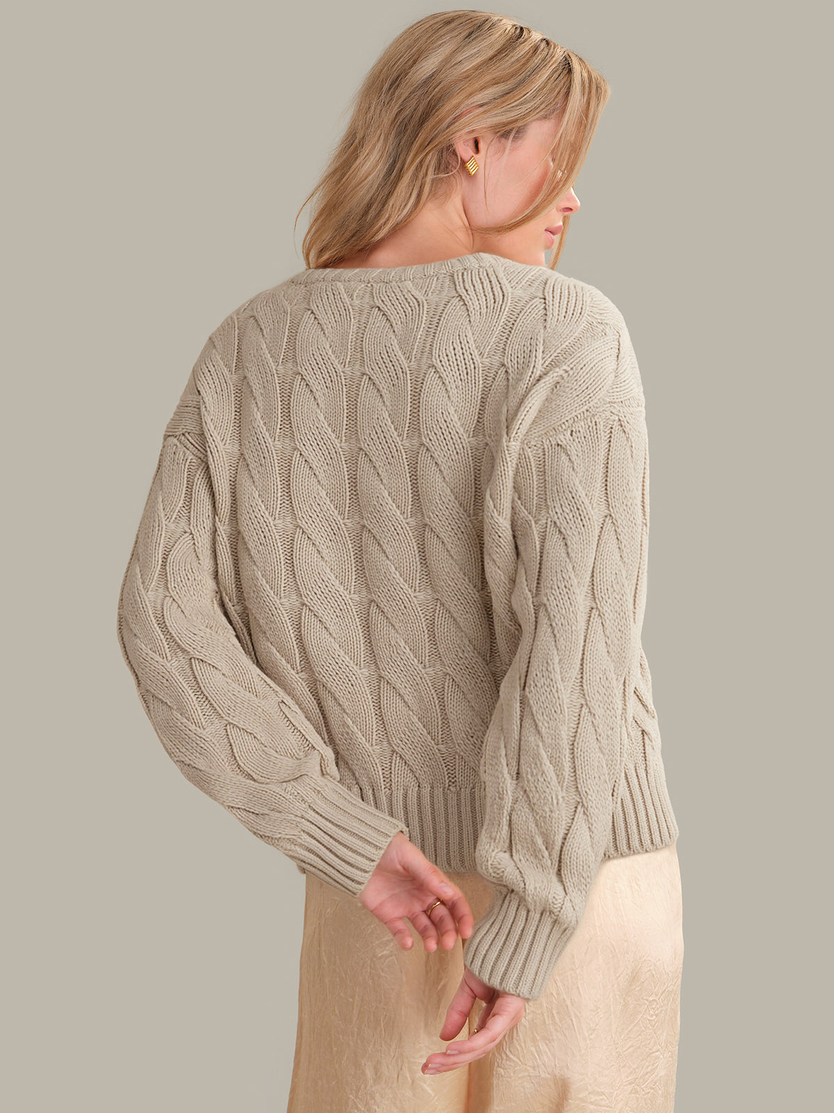 Woman wearing a beige cable knit sweater against a plain background
