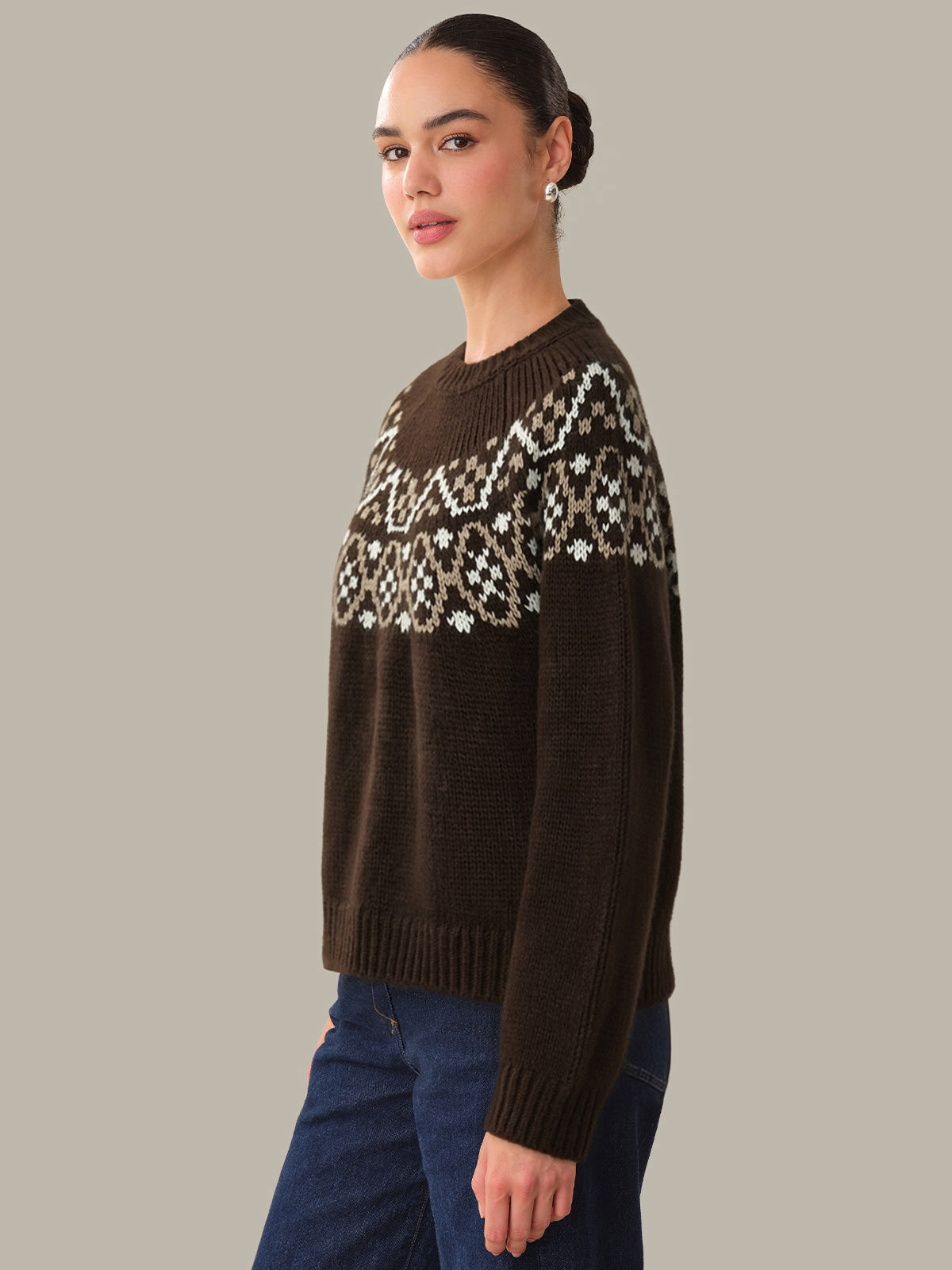 Woman wearing a brown sweater with a patterned yoke against a gray background