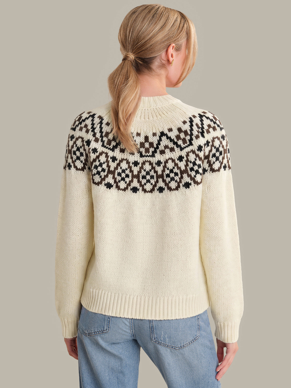 Person wearing a cream sweater with a black and white pattern on the back against a plain background