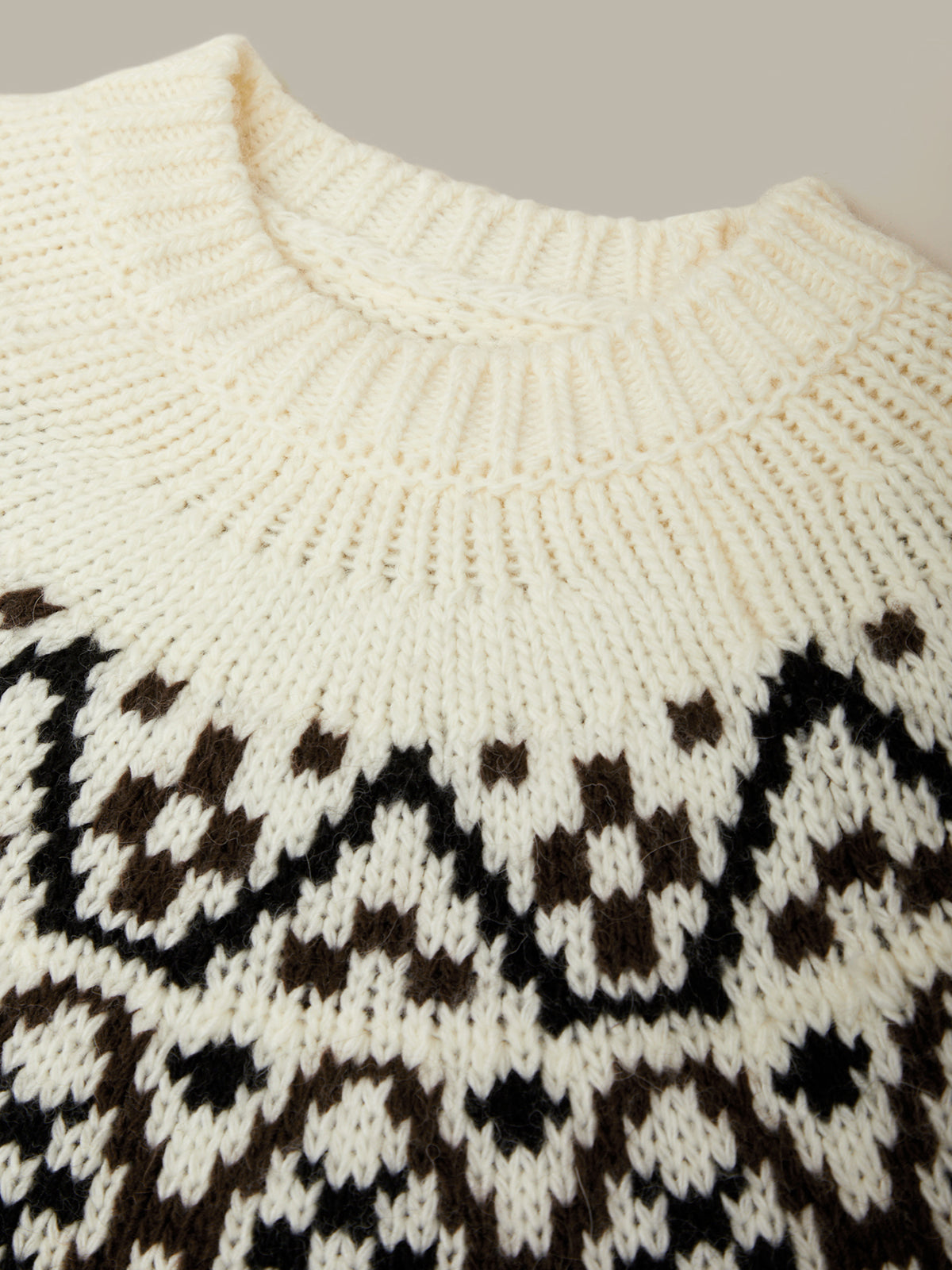 Close-up of a white knit sweater with black pattern on a neutral background