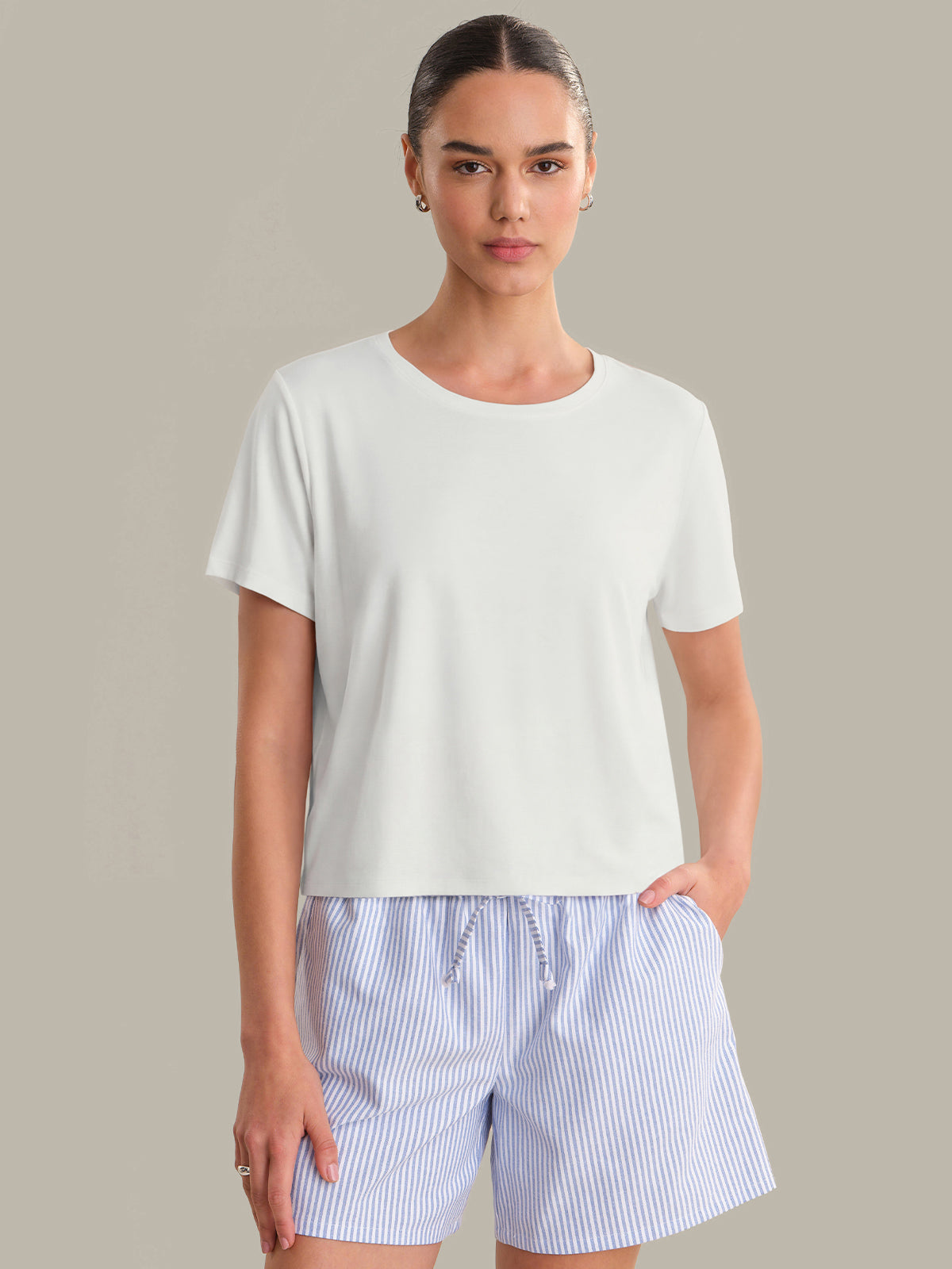 Woman wearing a white t-shirt and blue striped shorts on a beige background