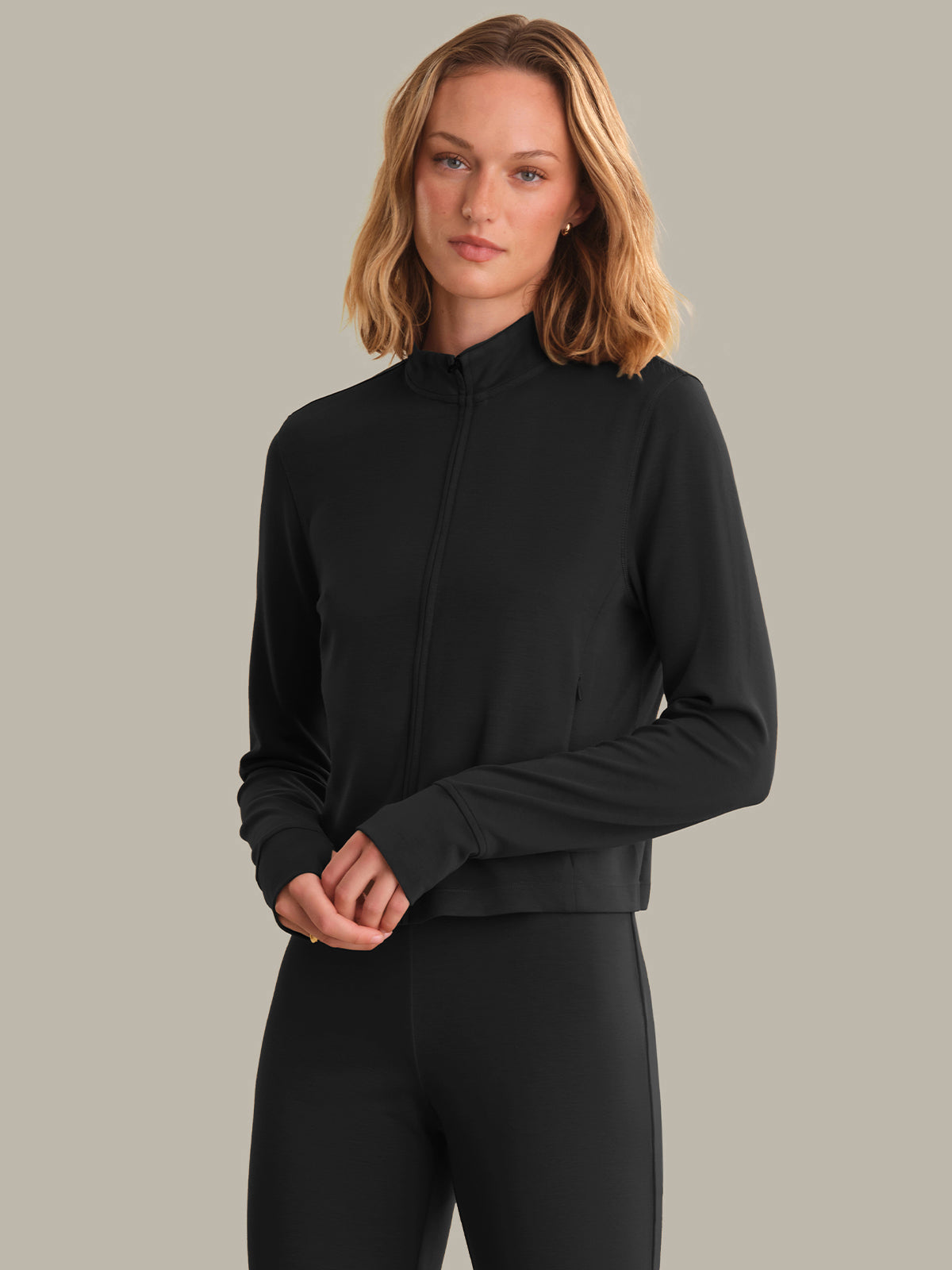 Woman wearing a black long-sleeve top and black pants against a gray background