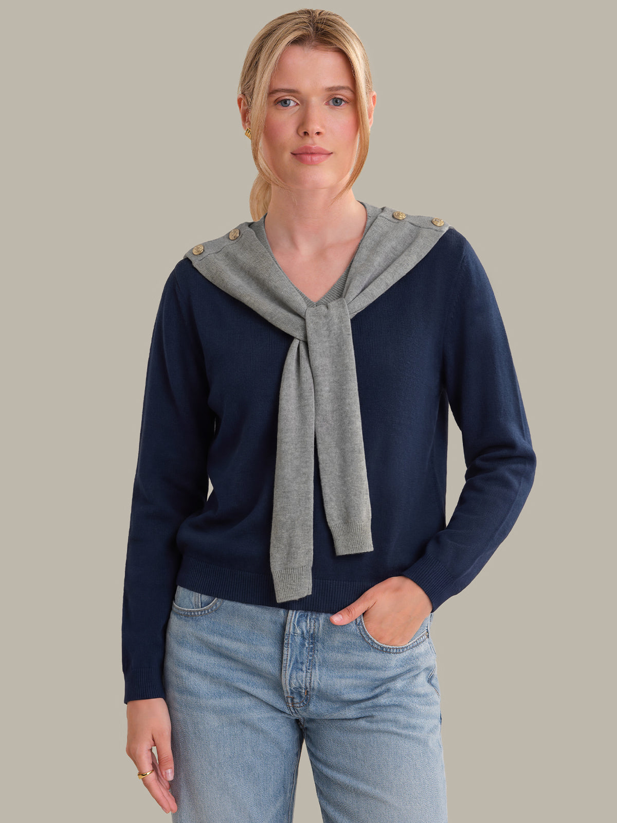 Woman wearing a navy sweater with a gray scarf against a neutral background