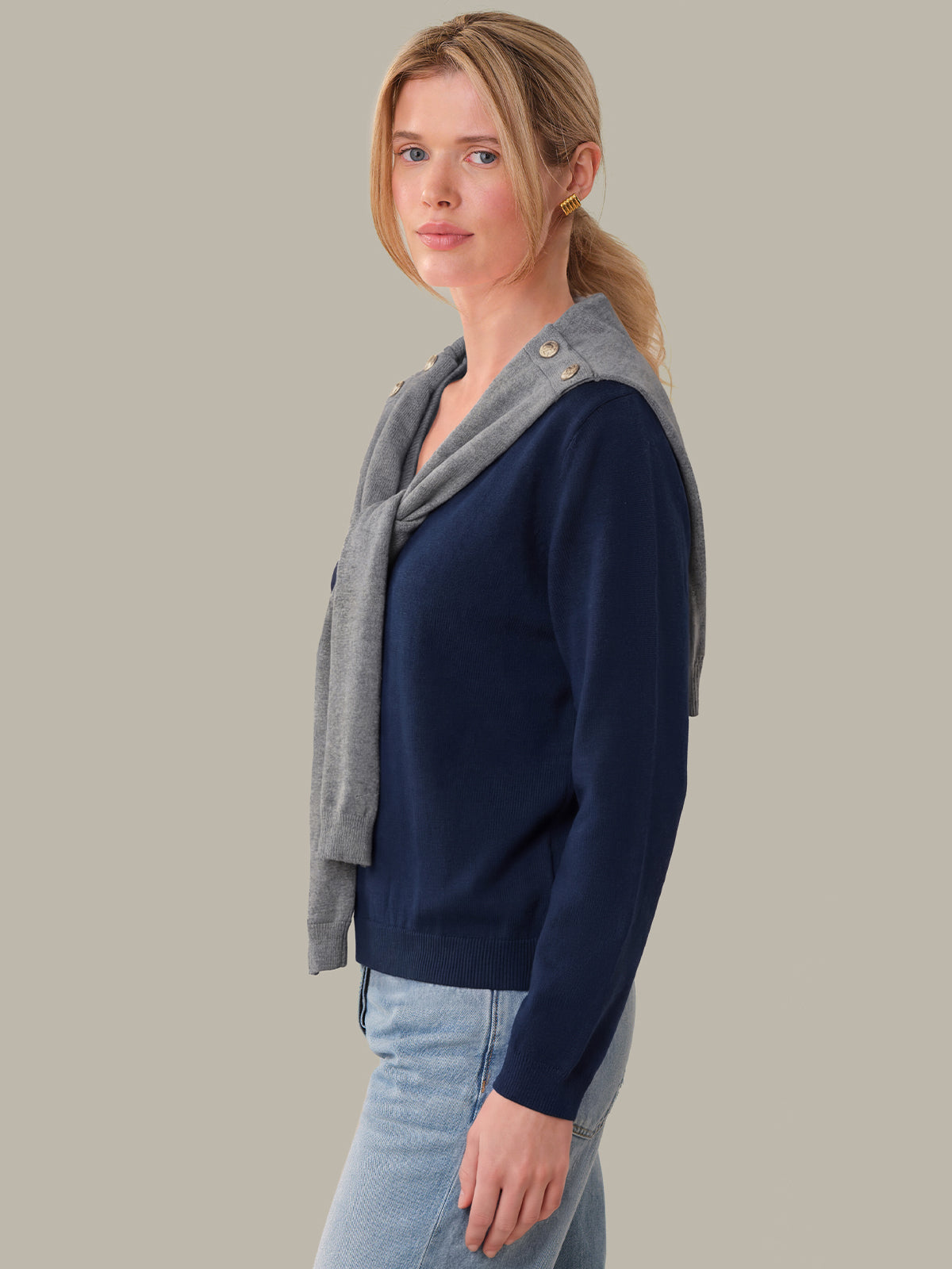 Woman wearing a navy sweater with a gray hood against a plain background