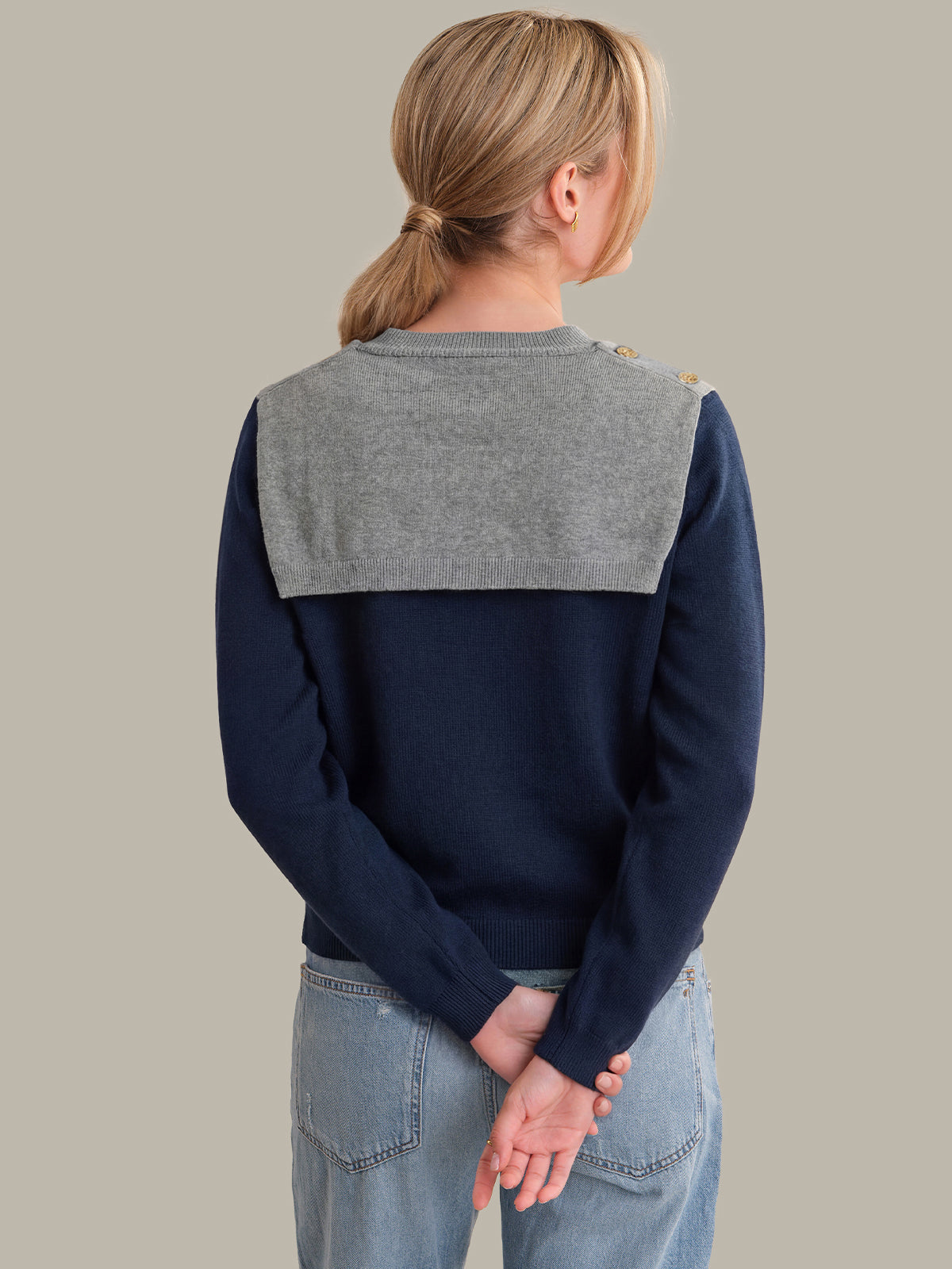 Person wearing a navy sweater with a gray collar against a plain background