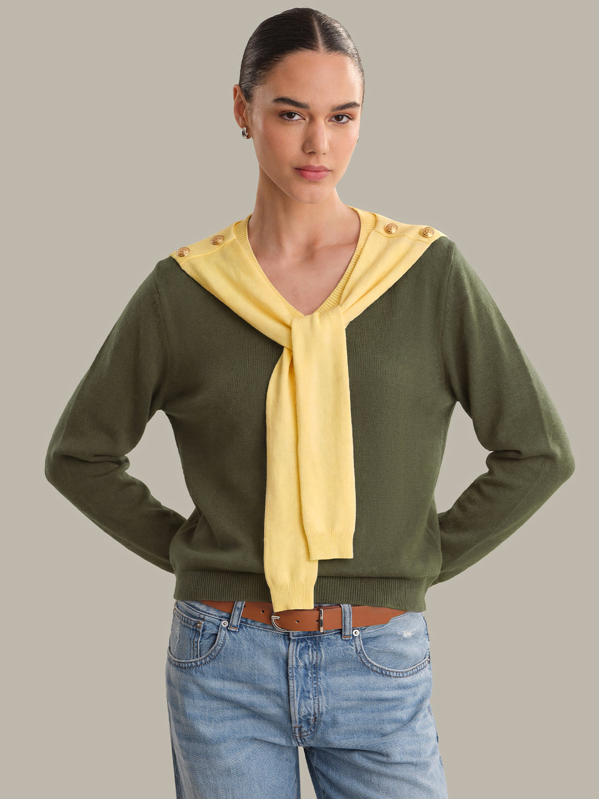 Woman wearing a green sweater with a yellow scarf against a gray background
