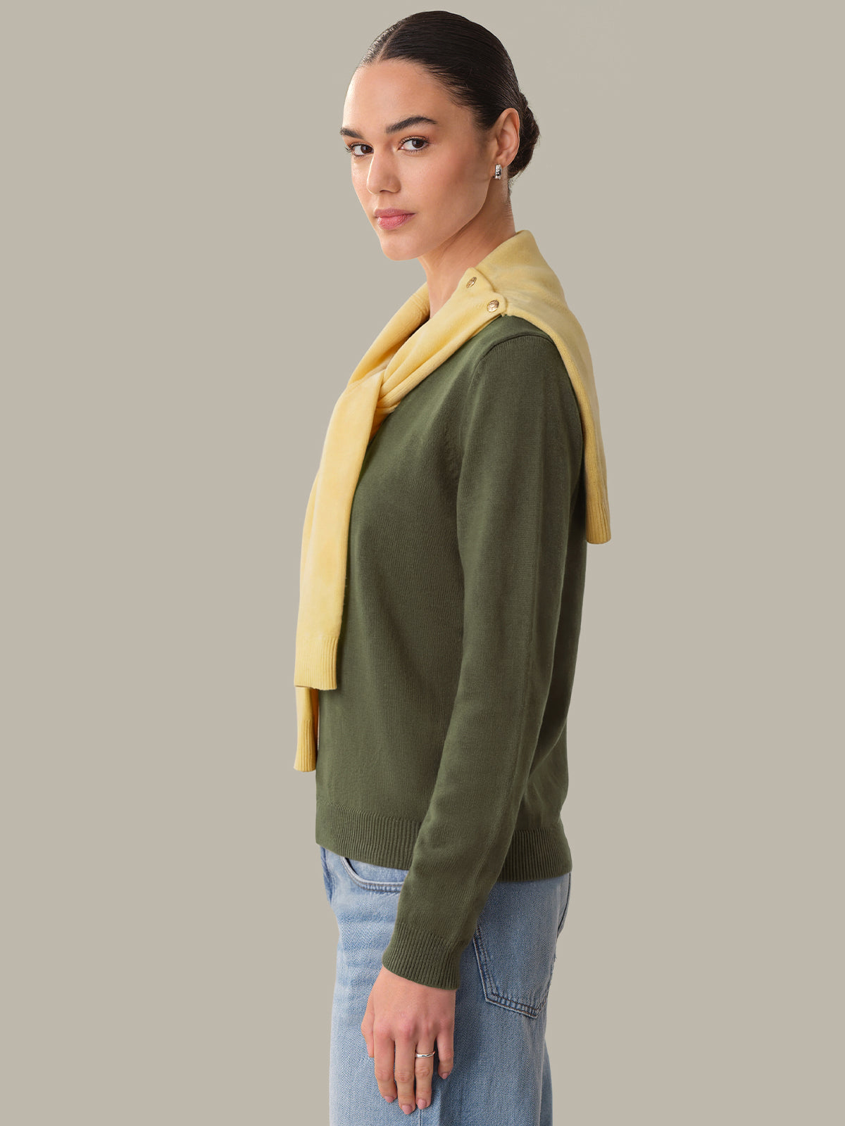 Woman wearing a green sweater and blue jeans with a yellow scarf on a gray background