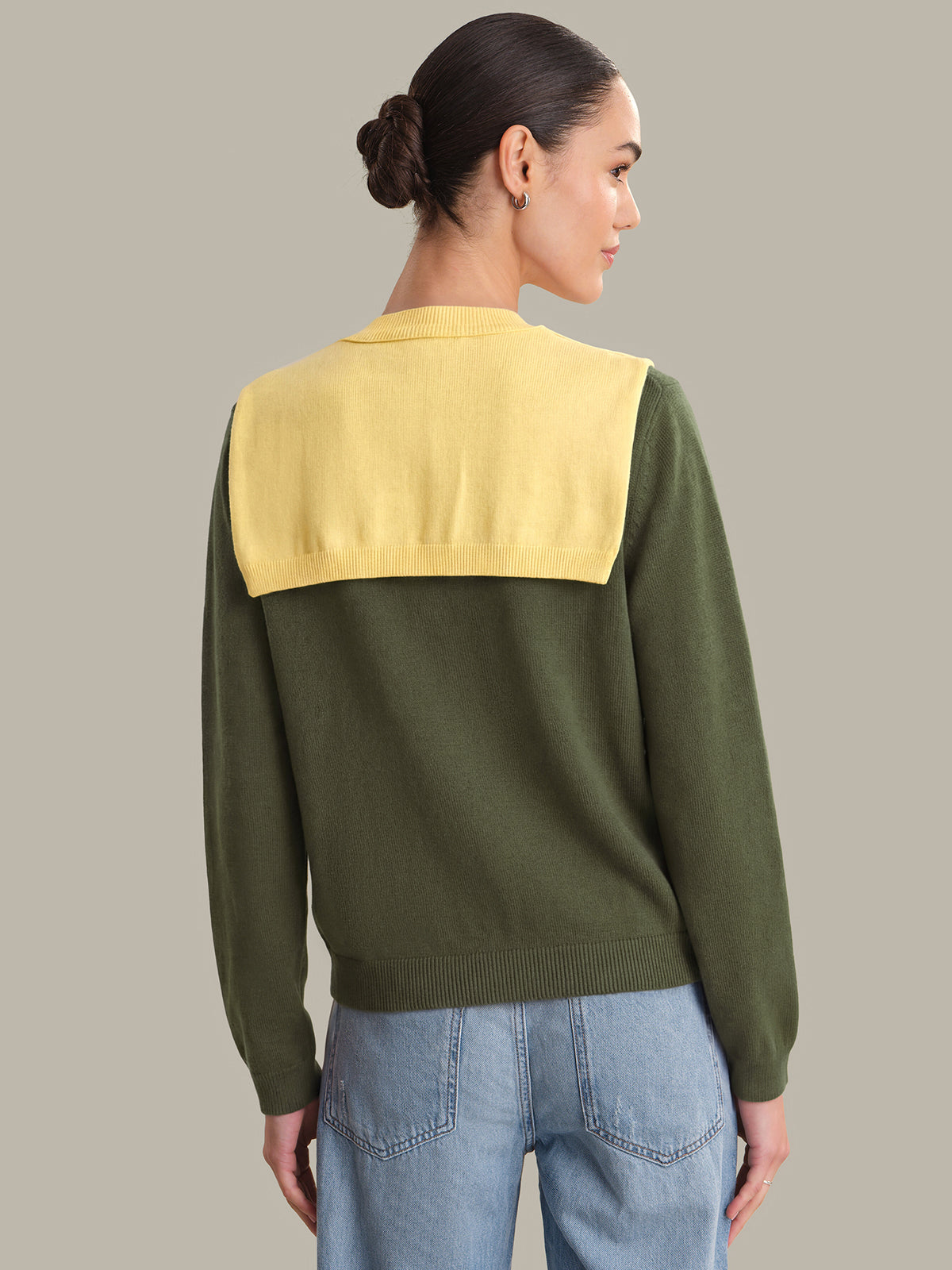Person wearing a green and yellow sweater with blue jeans on a neutral background