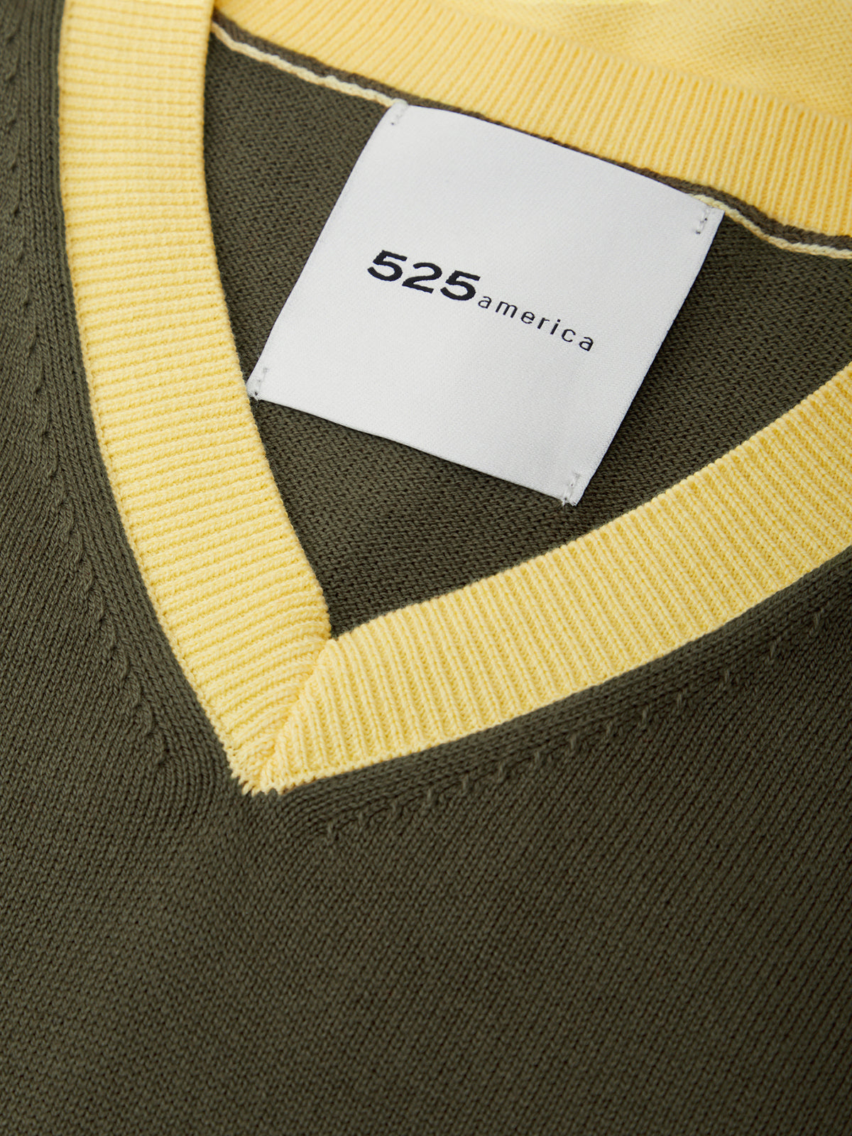 Close-up of a green sweater with a yellow trim and a visible brand label.