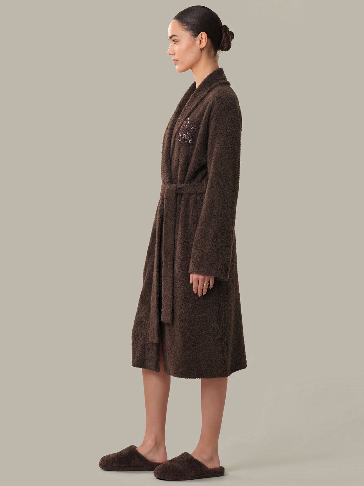 Woman wearing a brown robe with a logo on a plain background