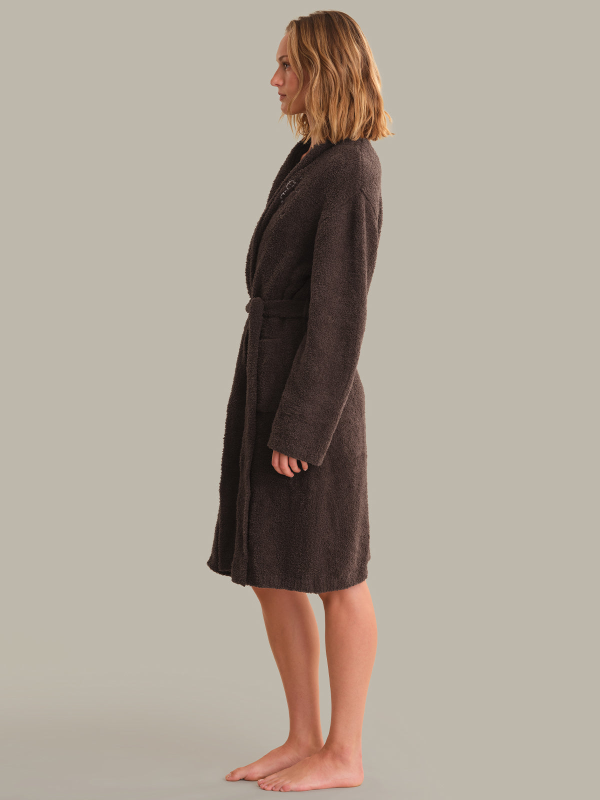 A woman wearing a dark brown plush bathrobe, shown in profile against a solid light gray background.
