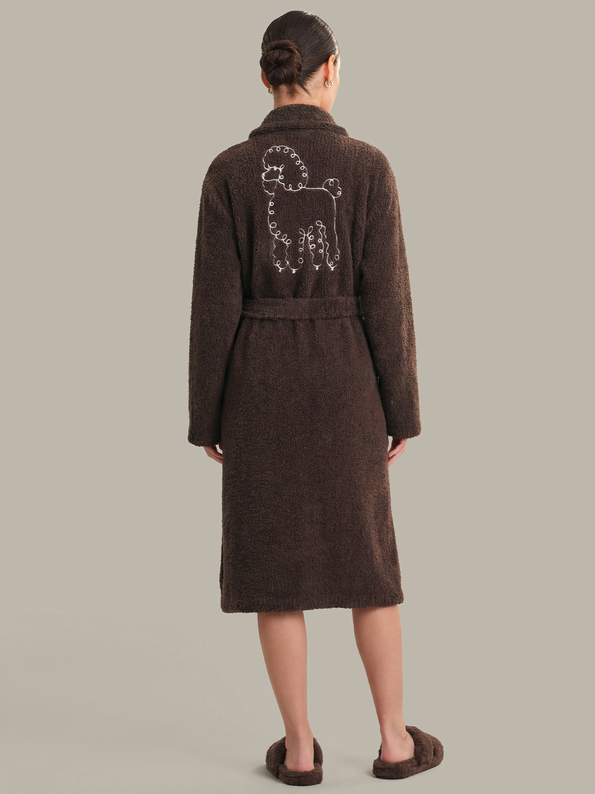 Person wearing a brown robe with a dog design on the back against a plain background