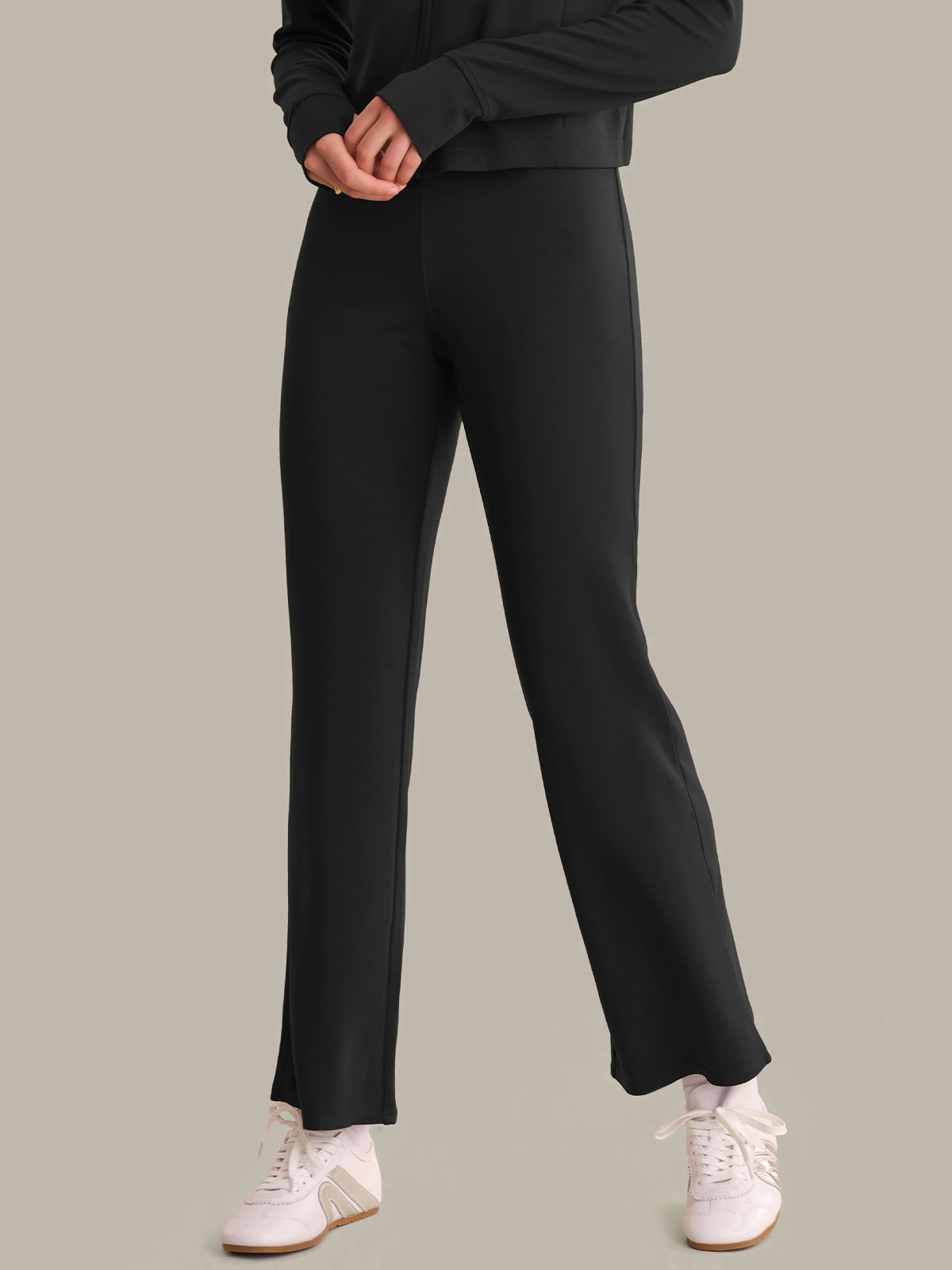 Person wearing black pants and white sneakers on a plain background