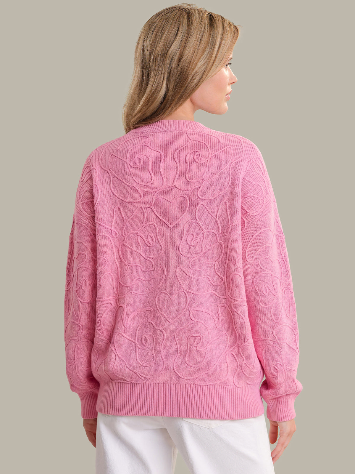 Woman wearing a pink sweater with floral patterns on a beige background