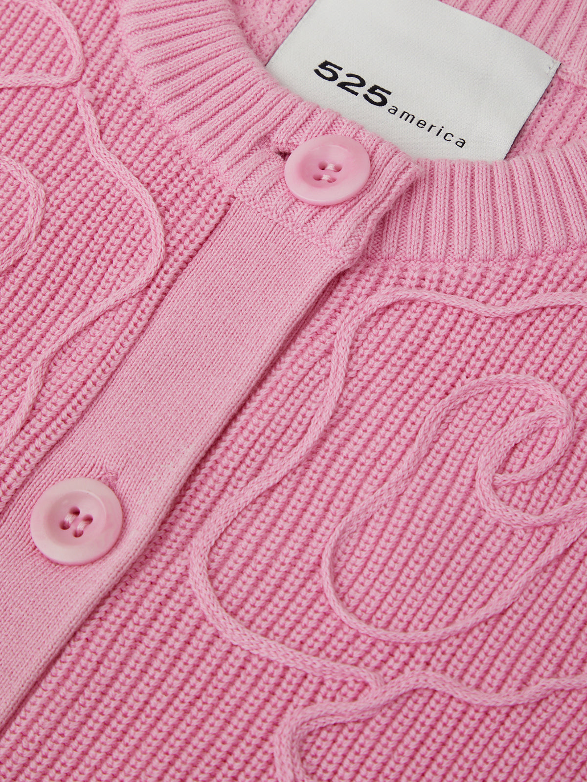 Close-up of a pink knitted cardigan with cable patterns and a brand label.