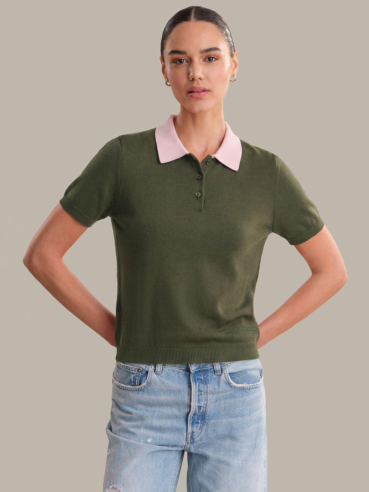 Woman wearing a green polo shirt with a pink collar and light blue jeans on a gray background