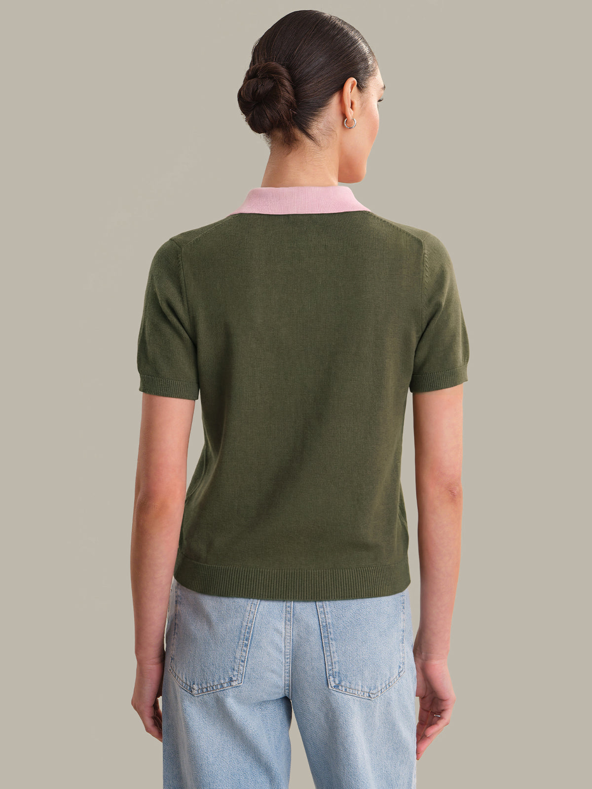 Person wearing a green sweater with a pink collar against a neutral background