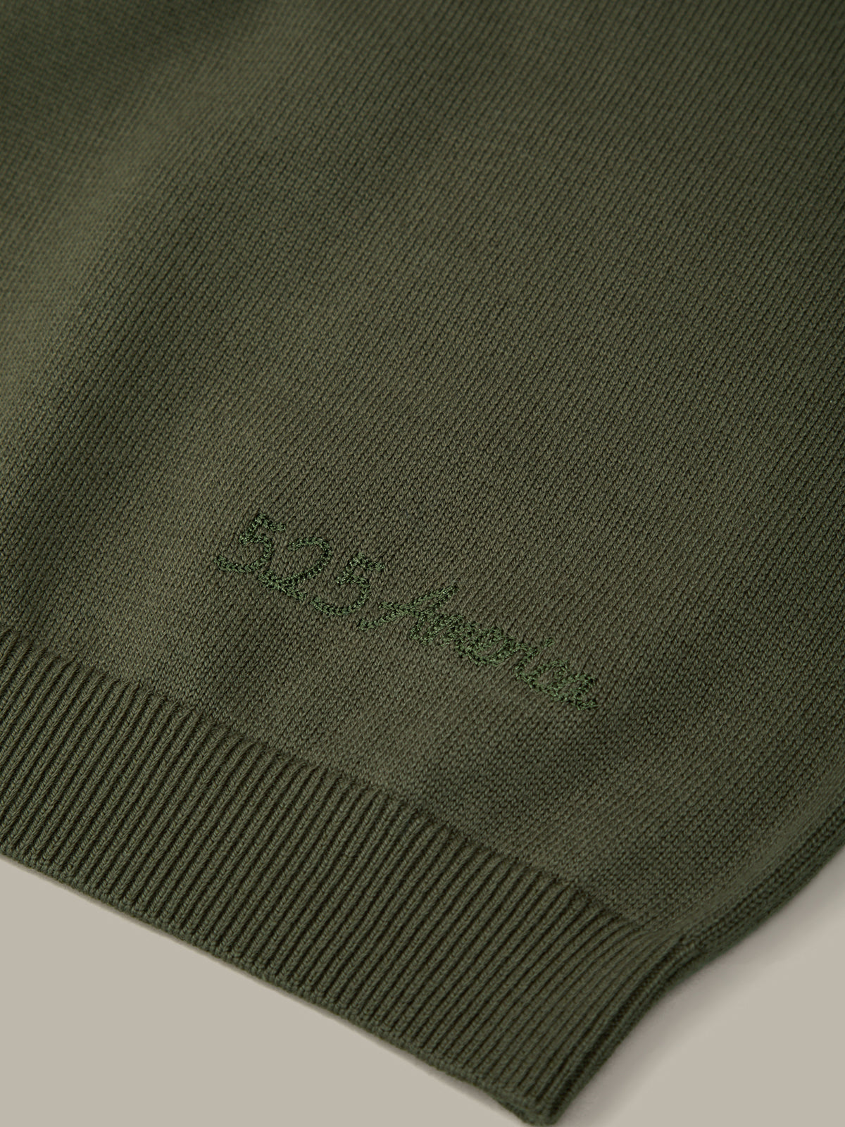Close-up of a green sweater with a brand logo on a light gray background