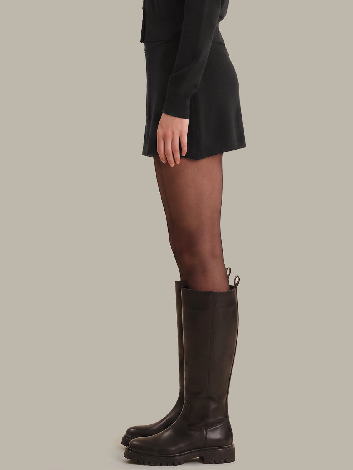 Brown knee-high boots worn with a black outfit on a neutral background