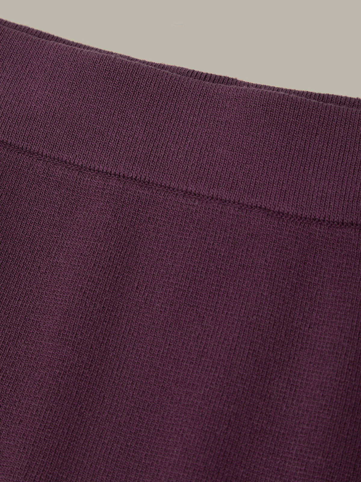 Close-up of a purple fabric with a visible seam on a beige background