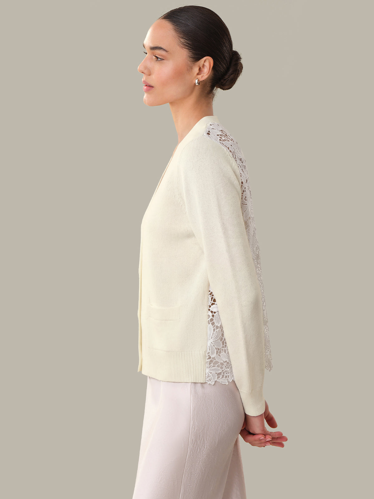 Woman wearing a light-colored jacket with lace details on a neutral background